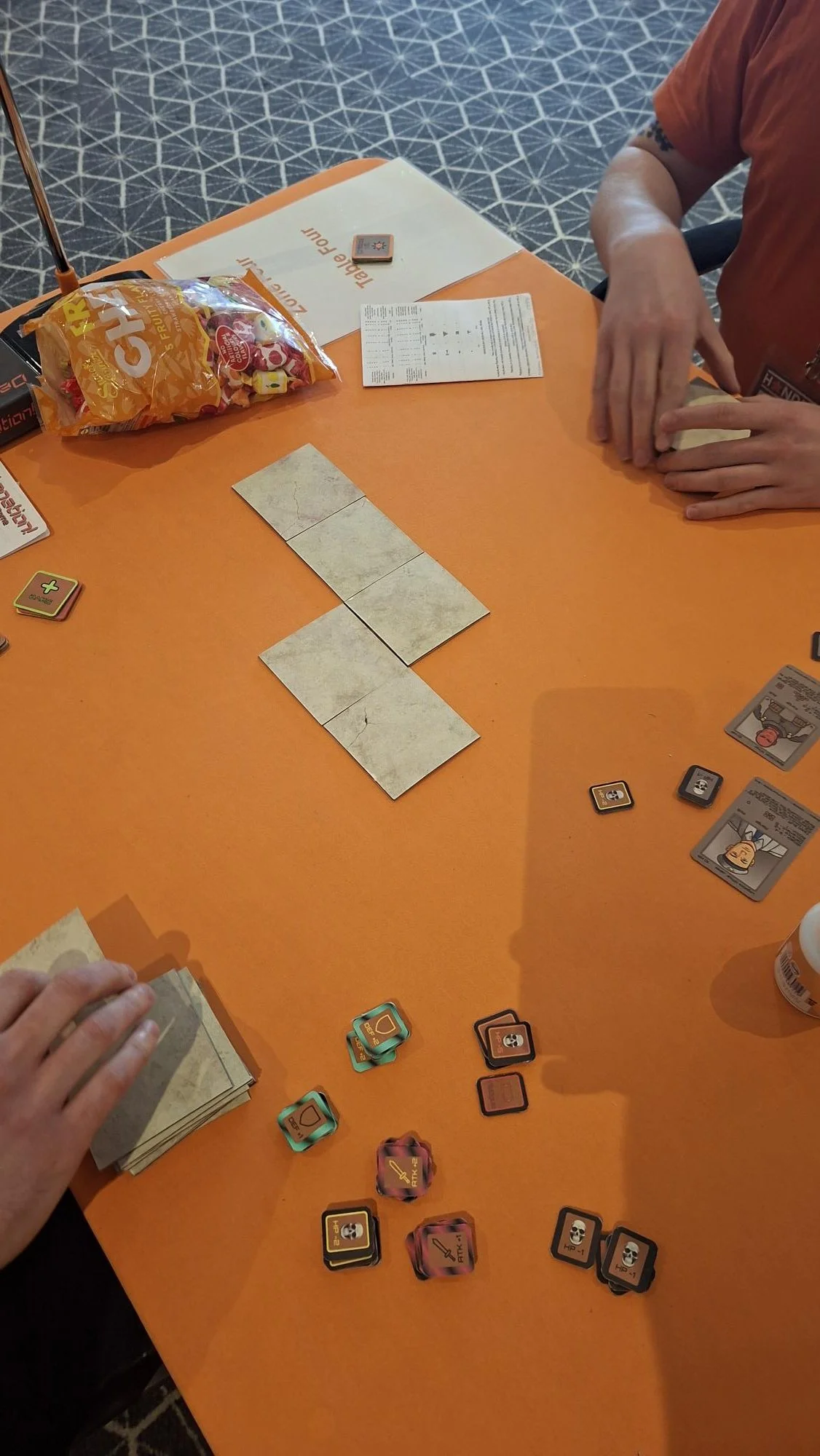 People playing the card game 'Detonation! The Card Game' at Handycon Jan 2026. a table with game pieces, cards, and instruction sheets.