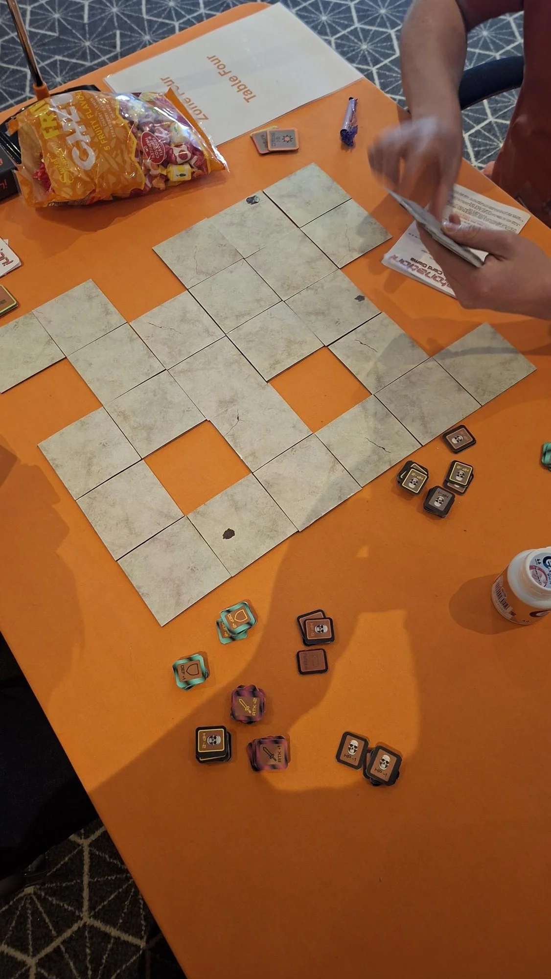 People playing the card game 'Detonation! The Card Game' at Handycon Jan 2026. a table with game pieces, cards, and instruction sheets.