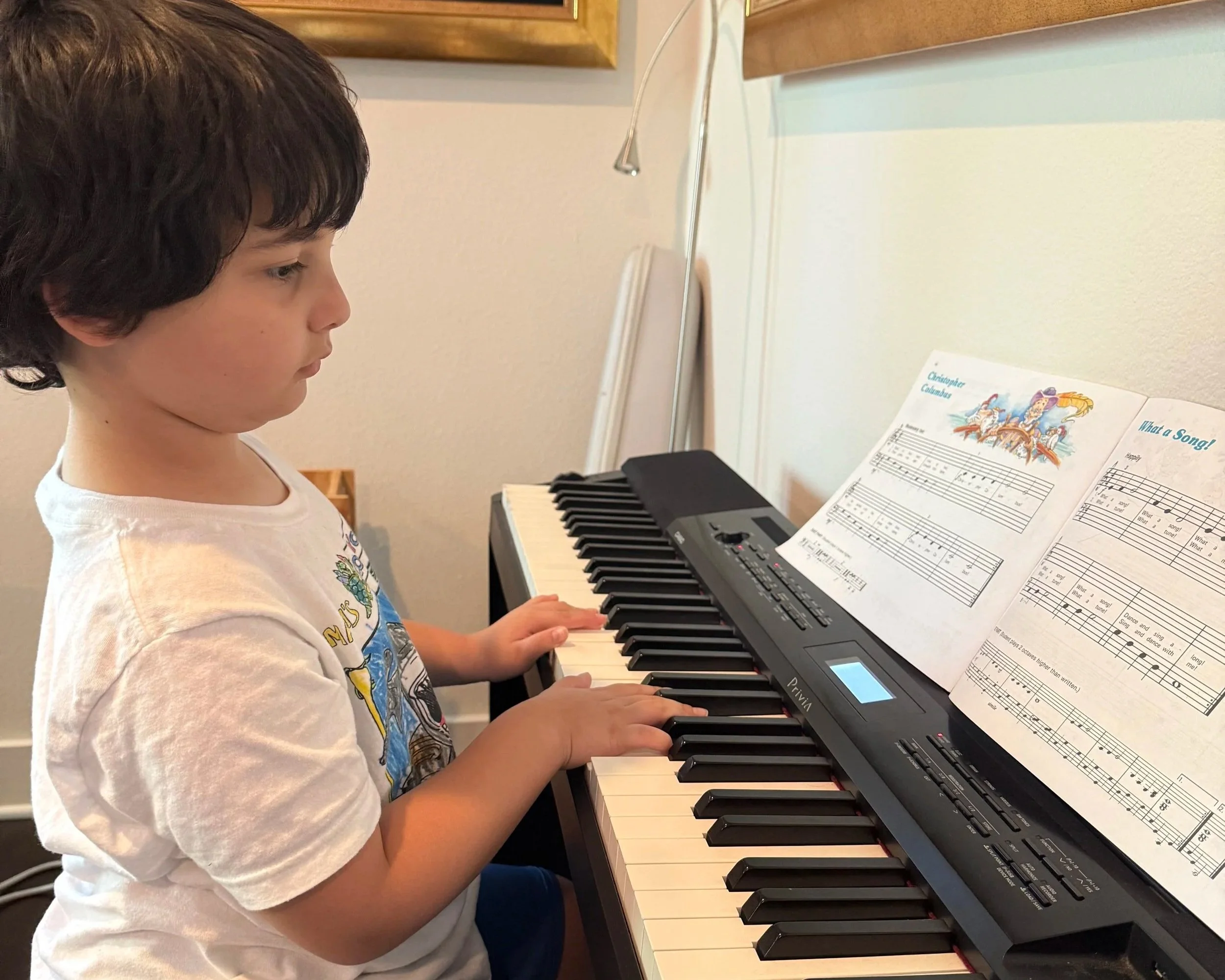 Little boy sits at piano and reads music.