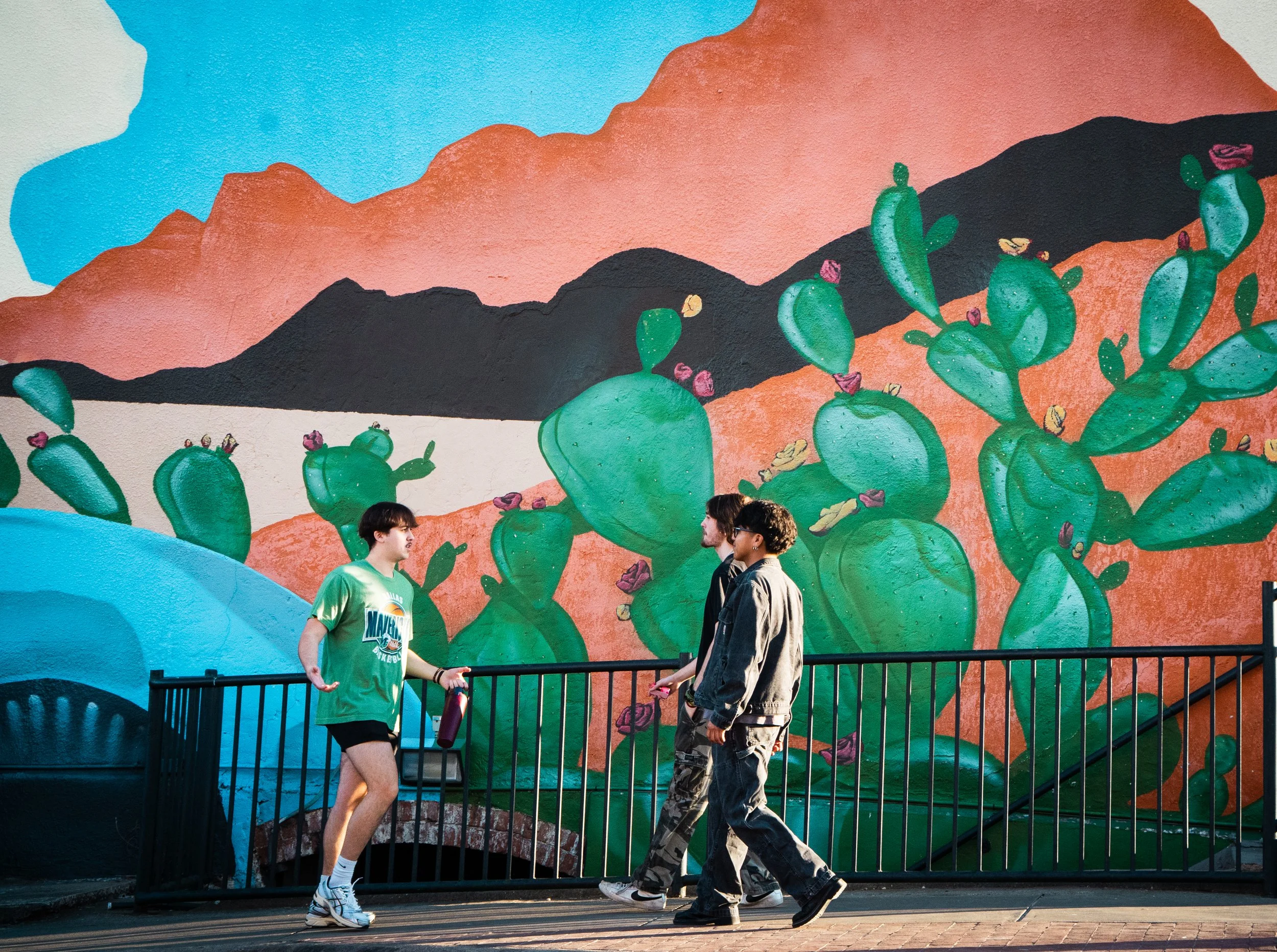 Cactus Crossing 
-
Denton residents Quinn Powers, Ryan Ondich, and Kevin Mesita walk along the square past Free Play's desert mural. Monday's sunshine allowed many residents to enjoy walks along the square as the city prepares for the spring.