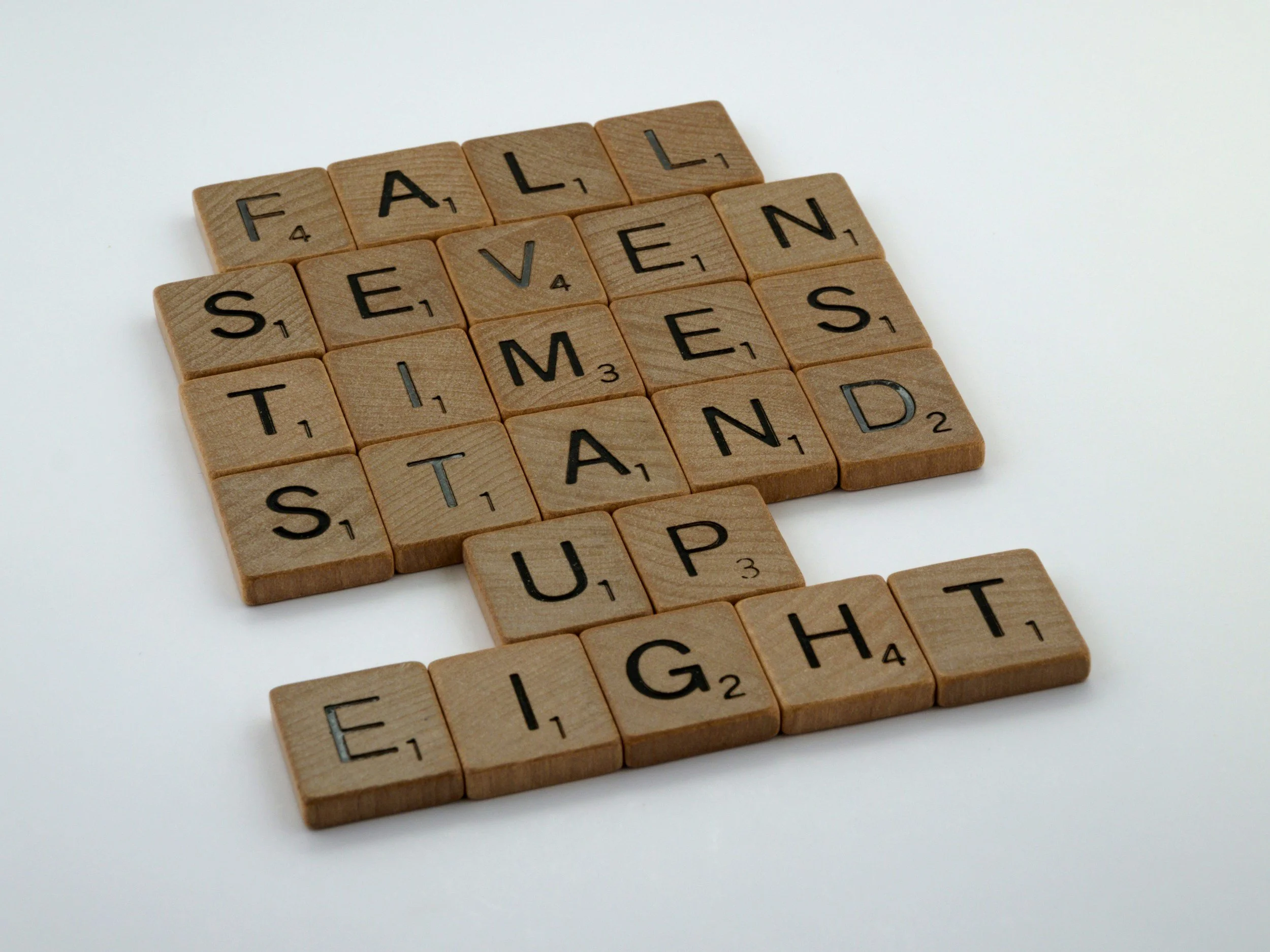 Scrabble tiles spelling out the phrase 'Fall Seven Start' on a white surface.