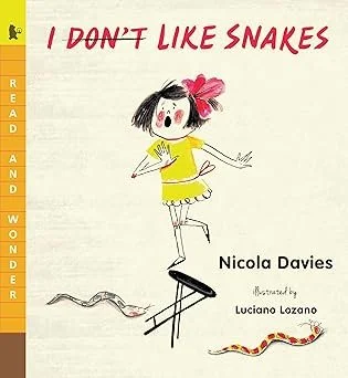Illustration of a girl with black hair, a pink bow, wearing a yellow dress, jumping over a snake, with the text 'I DON'T LIKE SNAKES' above her. Book title and author are at the bottom.