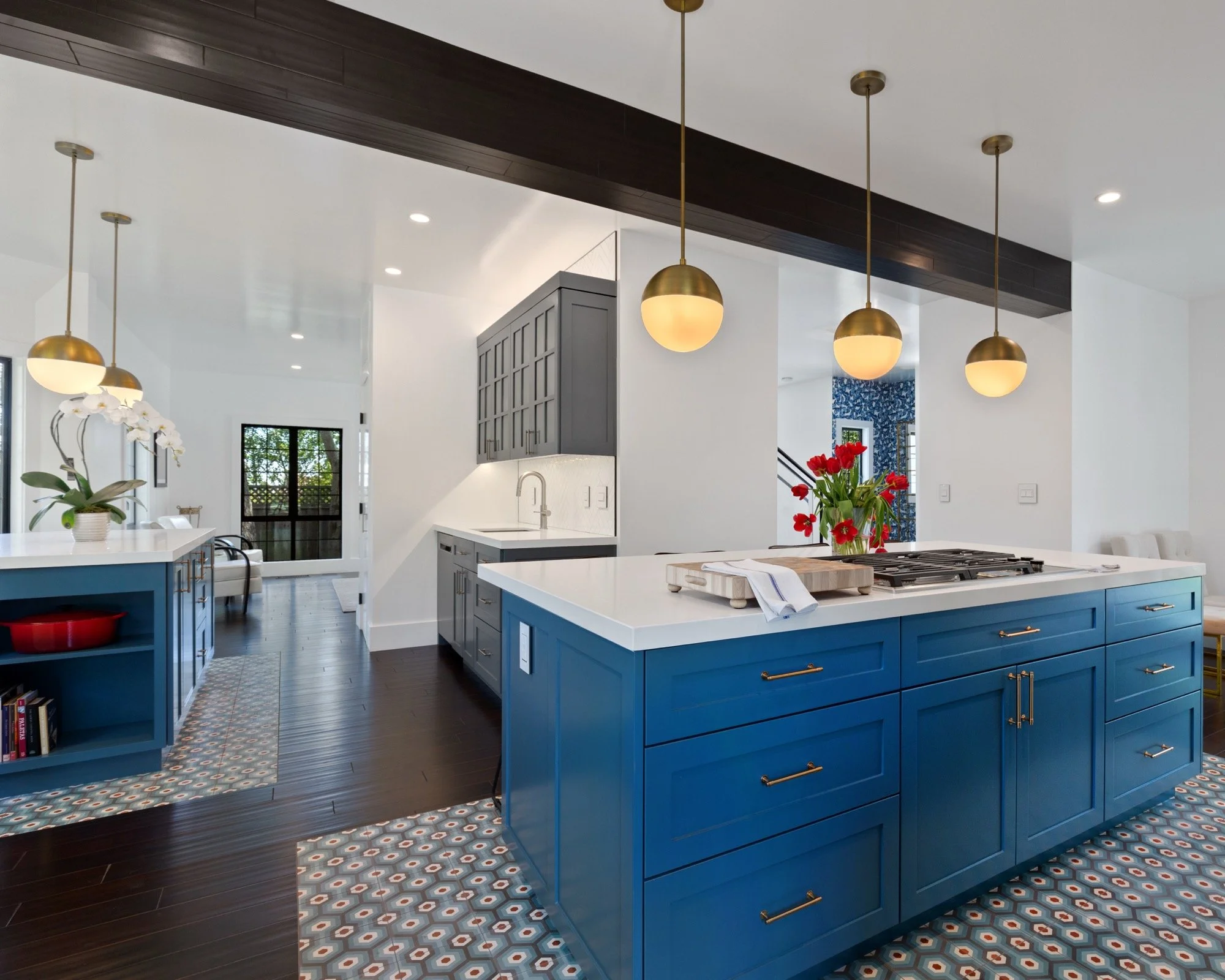 Modern kitchen with blue island, white countertops, dark wood flooring, pendant lights, and a vase of red flowers.