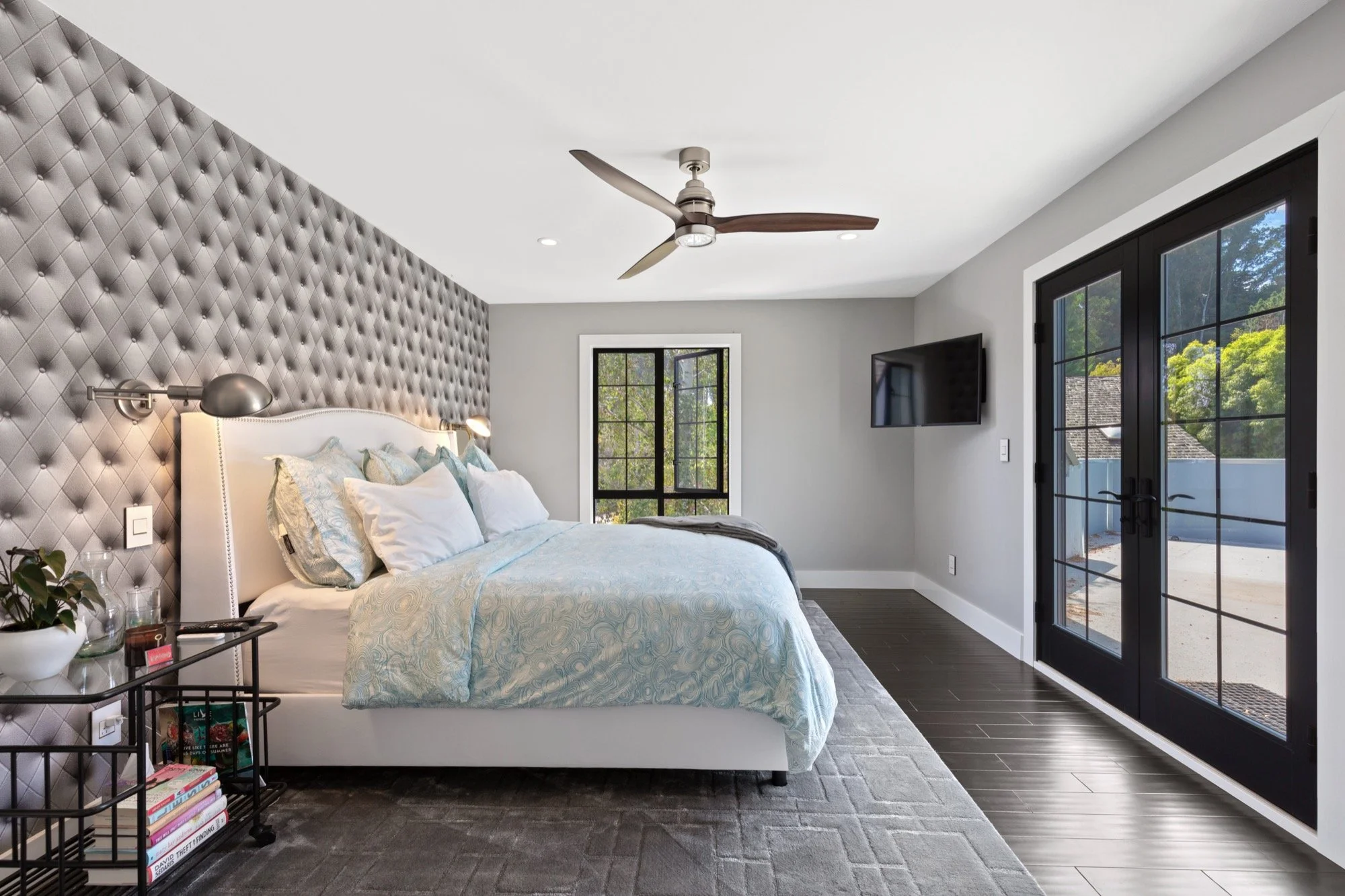 Modern bedroom with a large bed, textured gray accent wall, black-framed glass doors, and a wall-mounted TV.