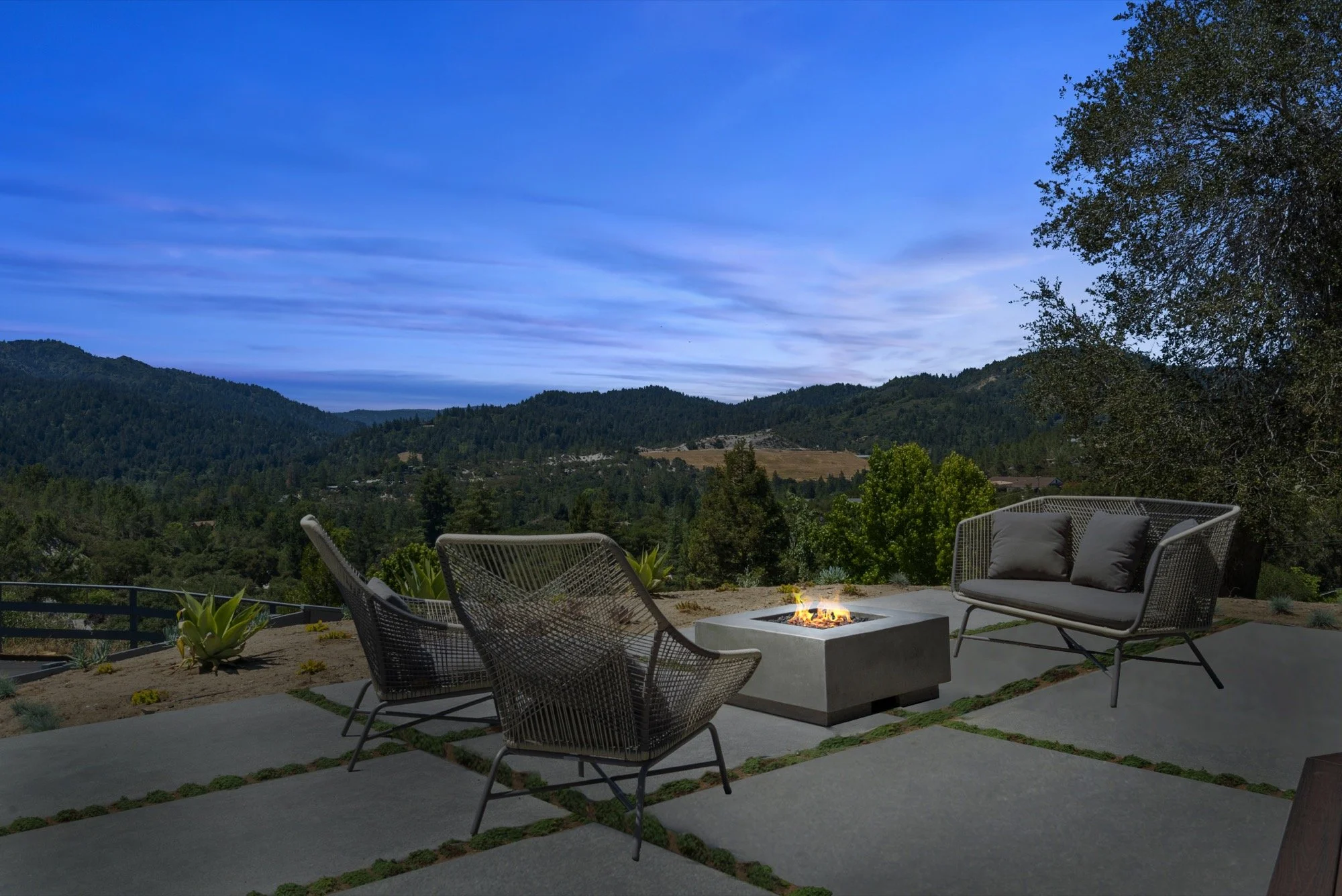 Outdoor patio with modern furniture and firepit overlooking a mountain landscape at dusk