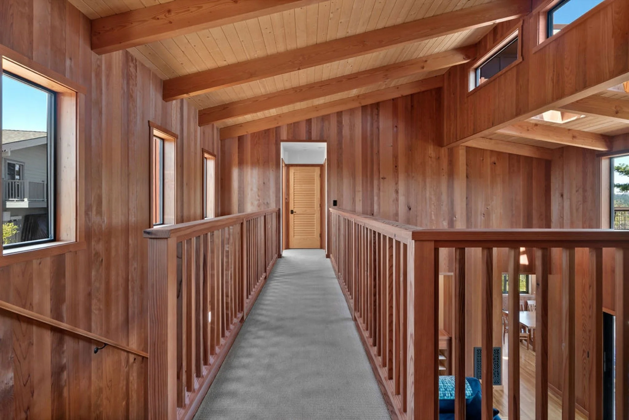 Wood-paneled hallway with a sloped ceiling, multiple windows, and a door at the end.