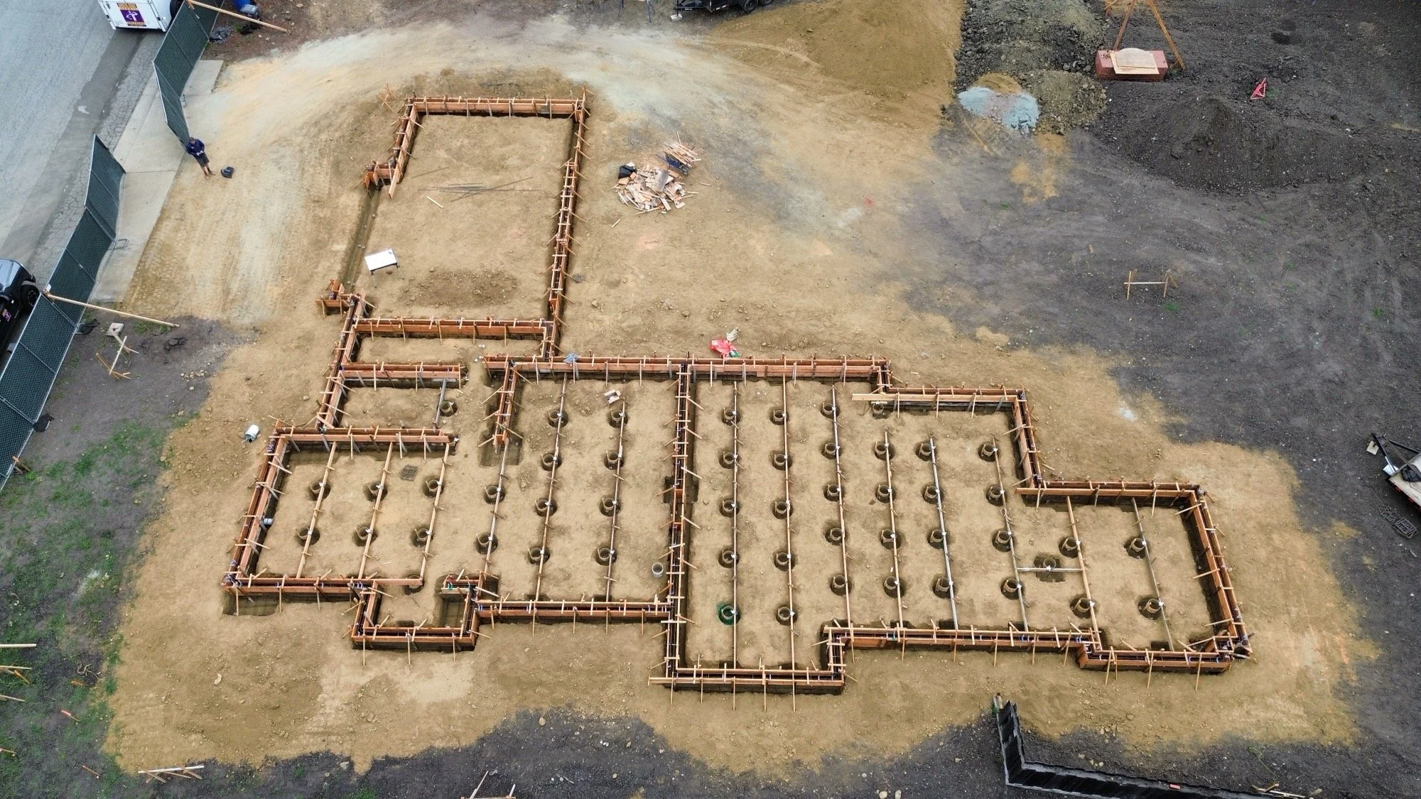 A construction site with the foundation for a building laid out with wooden forms and concrete piers, viewed from above.