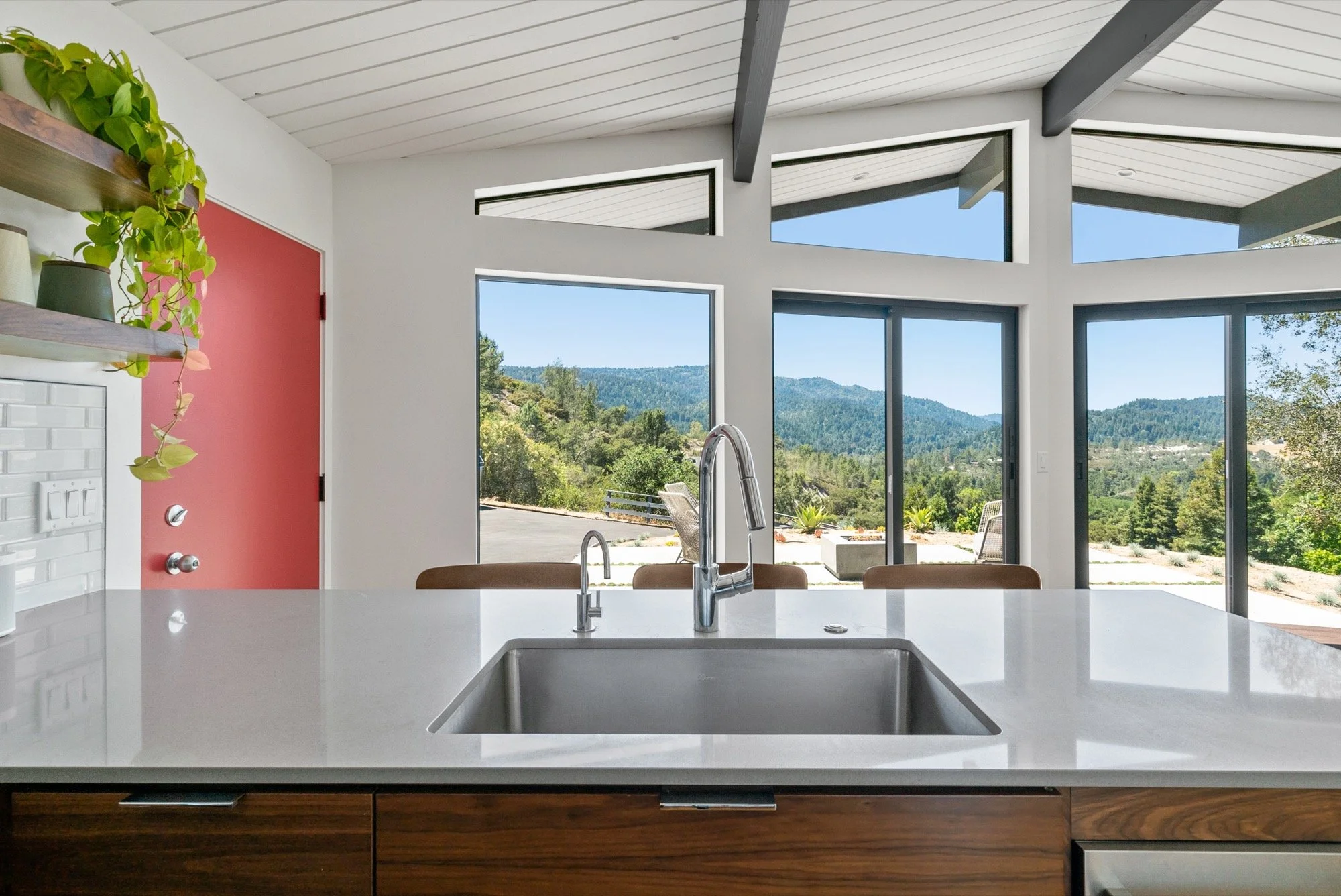 Modern kitchen with white countertops, a built-in sink, and large windows showcasing a mountain view and outdoor patio.