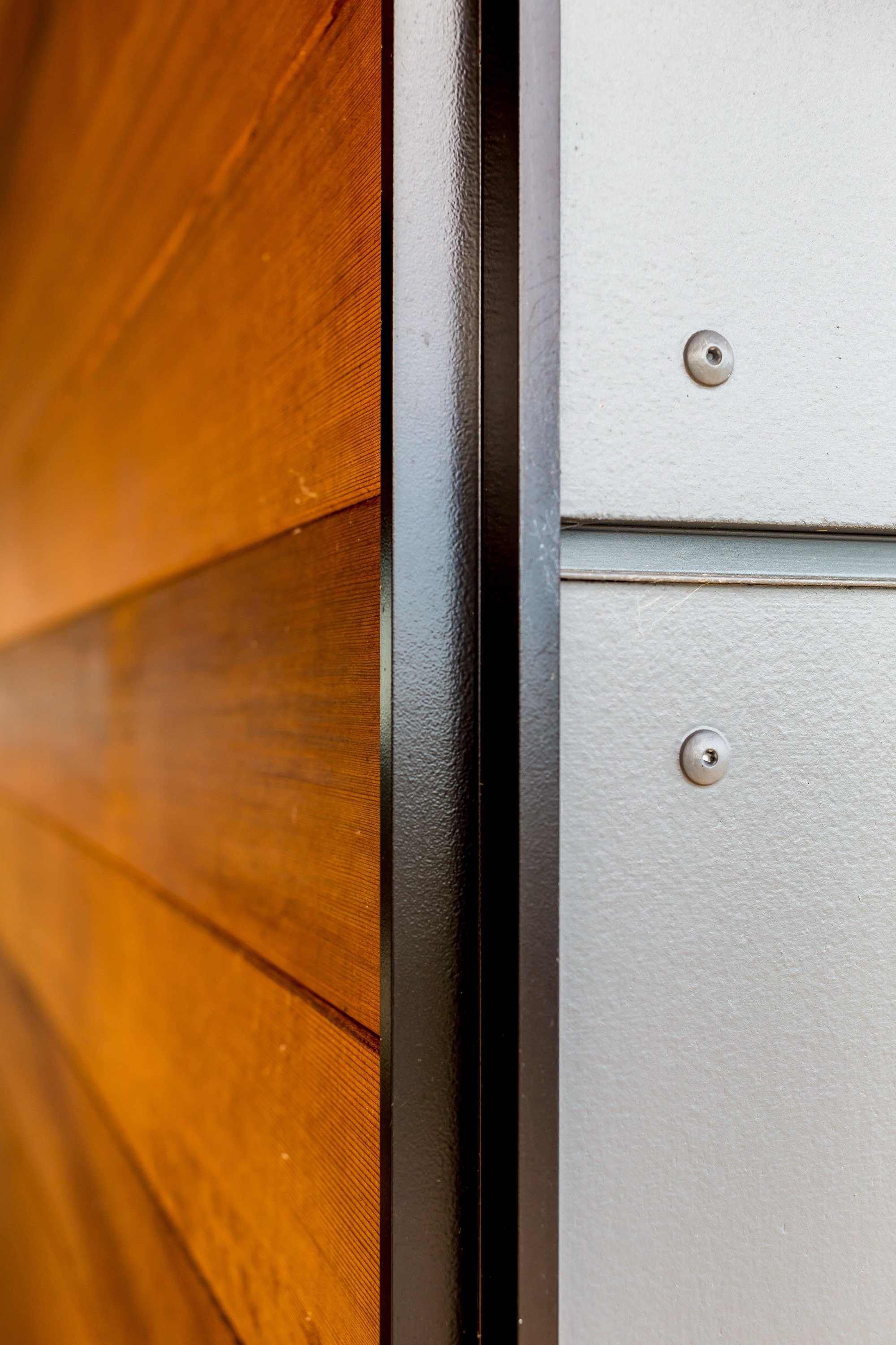 Close-up of a door frame with wooden paneling on the left and a white metal surface with screws on the right.