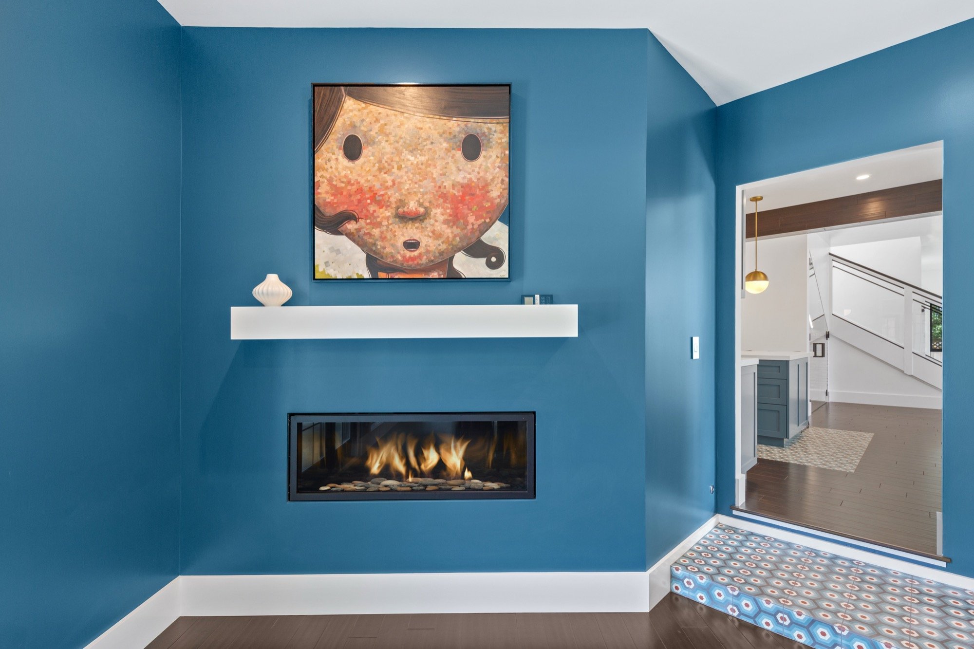 Living room with blue walls, a modern fireplace, abstract artwork, and decorative items on a white shelf.