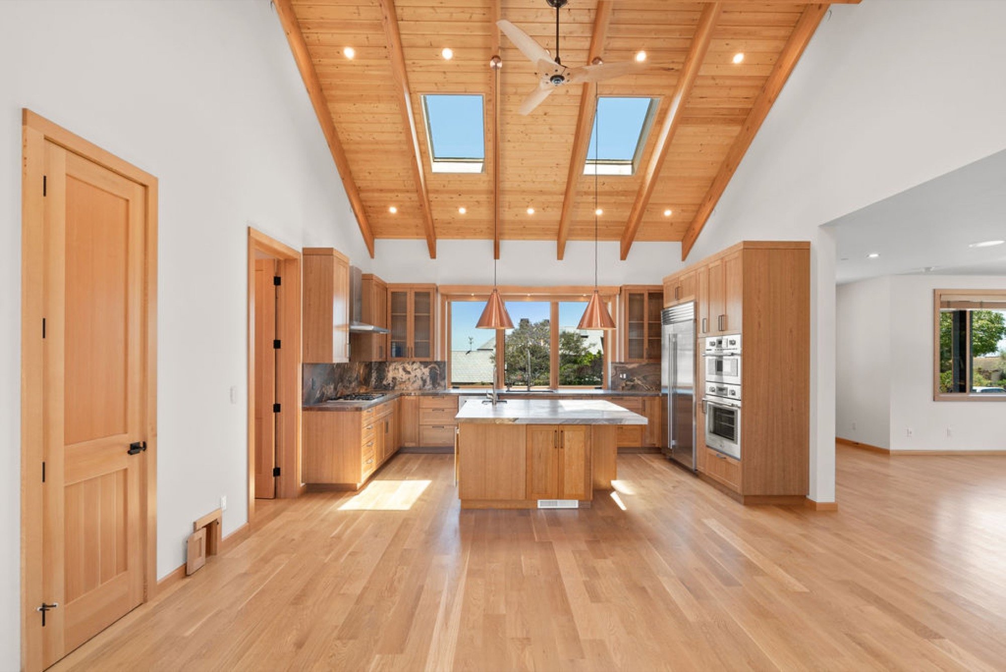 Spacious kitchen with wooden cabinets, a central island with a marble countertop, and skylight windows in a vaulted wooden ceiling.