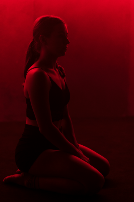 A woman kneeling in a dark room illuminated by red lighting, with her profile visible.