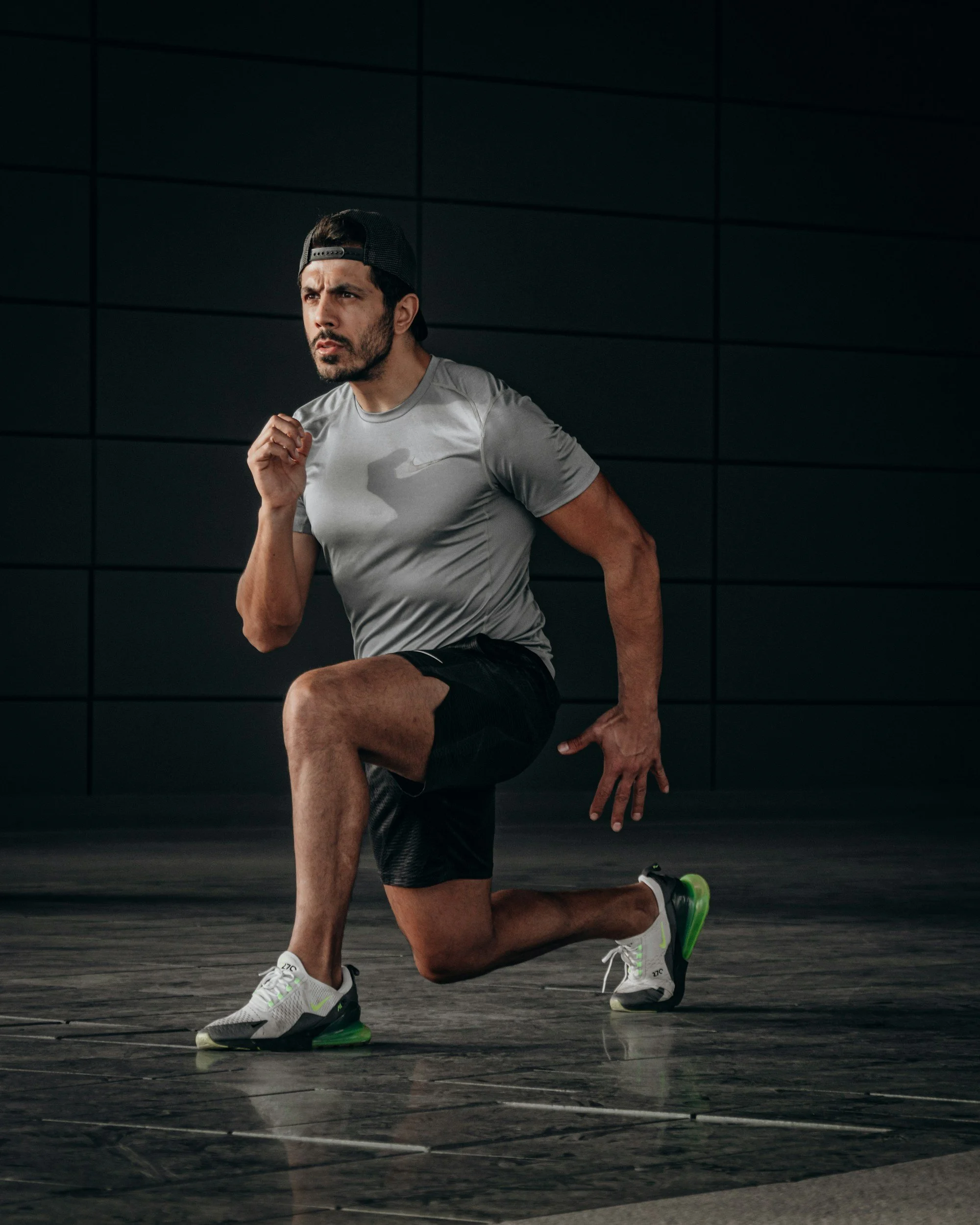 A man in athletic wear running indoors on a black tiled floor.