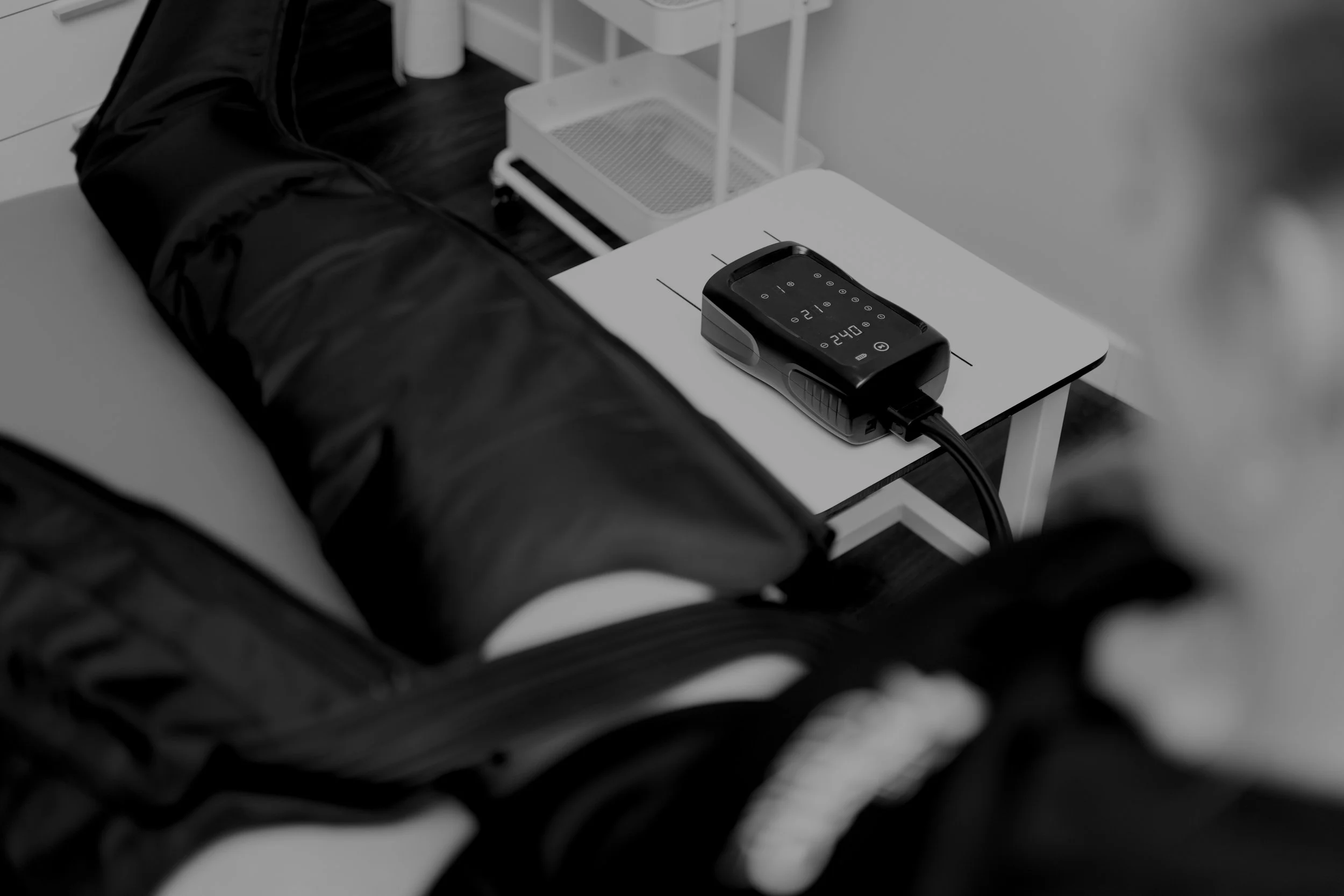 A person lying on a medical examination table with a cuff wrapped around their thigh, connected to a monitor on a nearby table, which displays temperature readings.