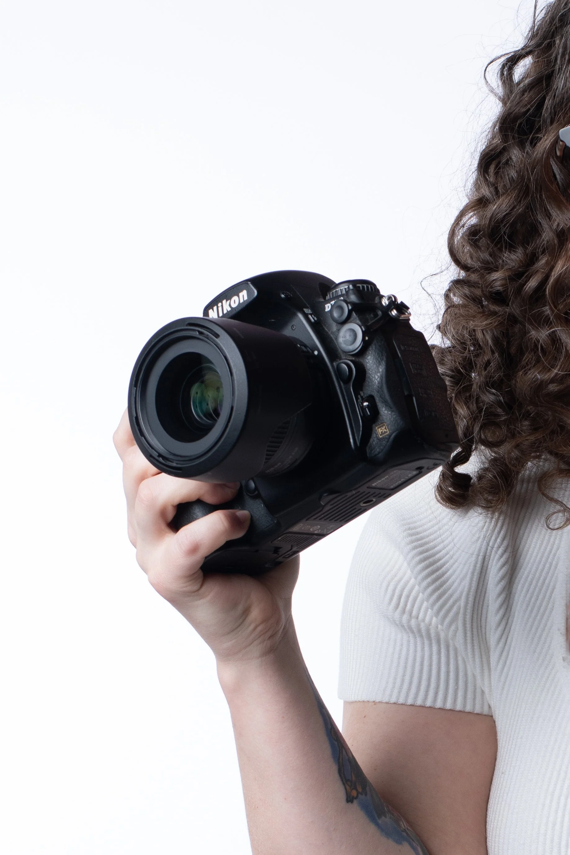 A woman with curly brown hair holding a black Nikon digital camera.