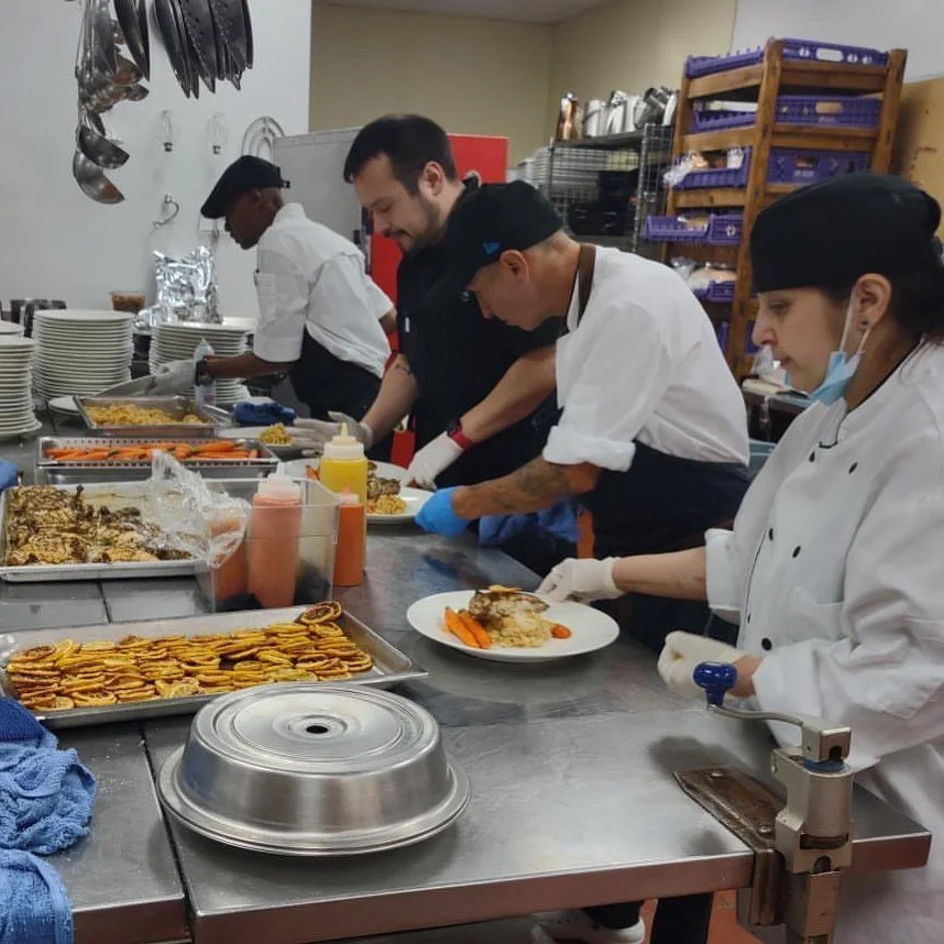 Chefs prepare and plate food in a kitchen with various dishes and utensils on the counter.
