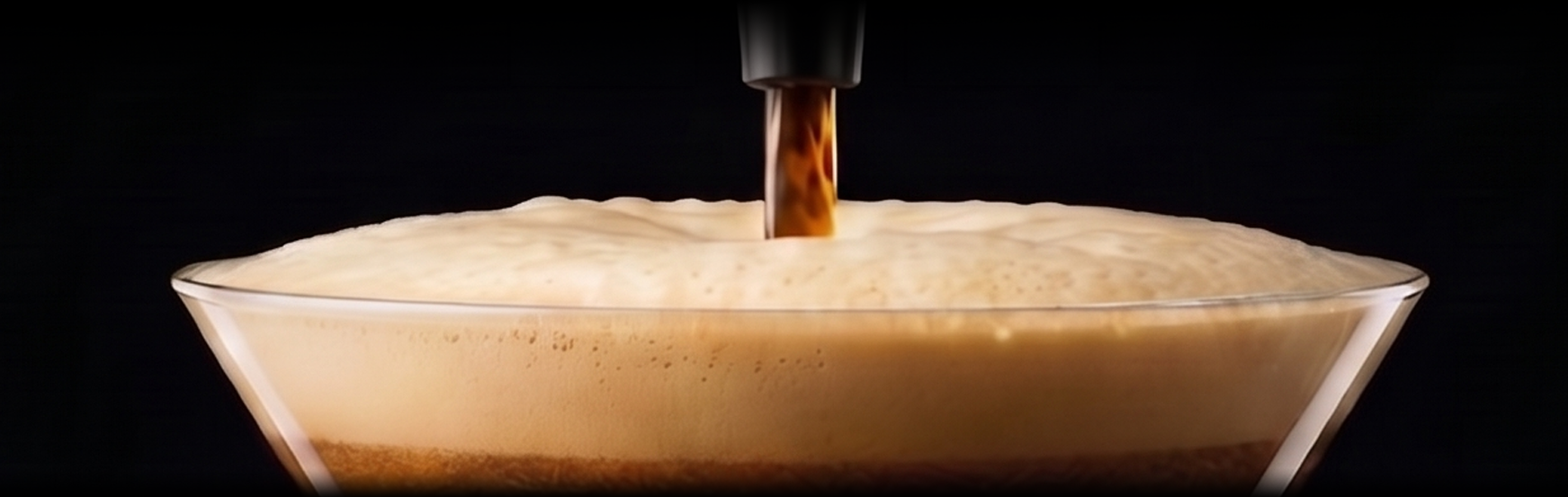 A martini glass with coffee foam being poured into it from above.