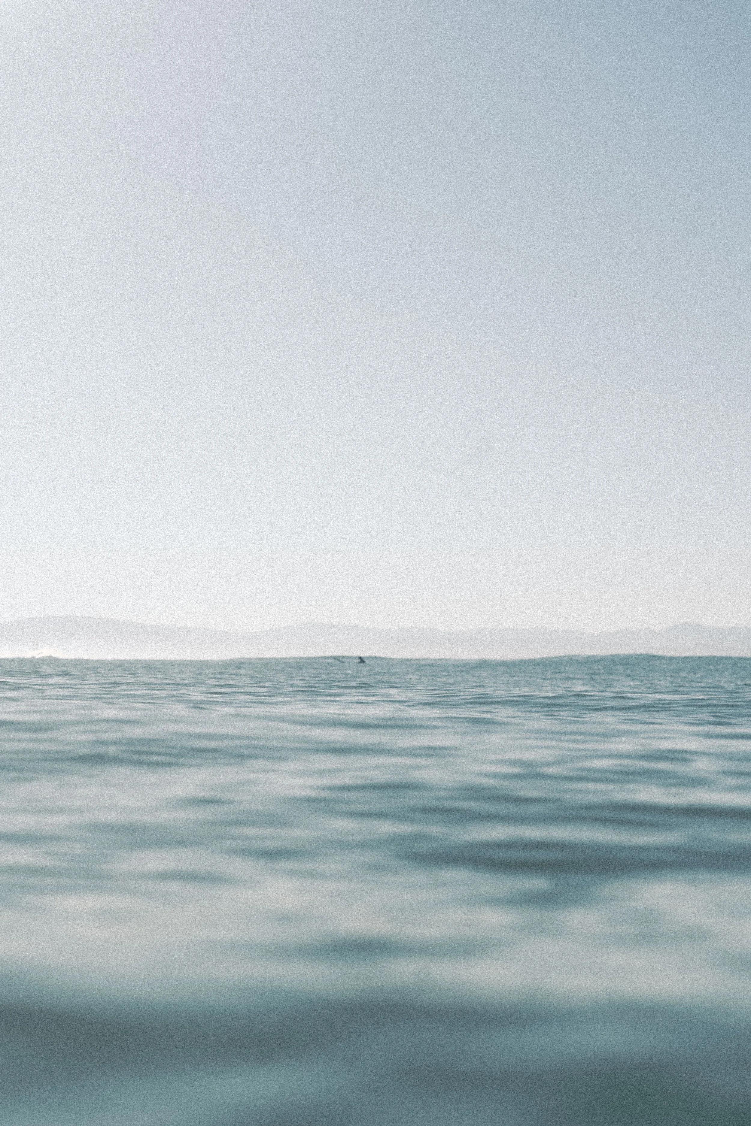 Calm ocean with gentle waves, distant mountains, and a light-colored sky overhead.