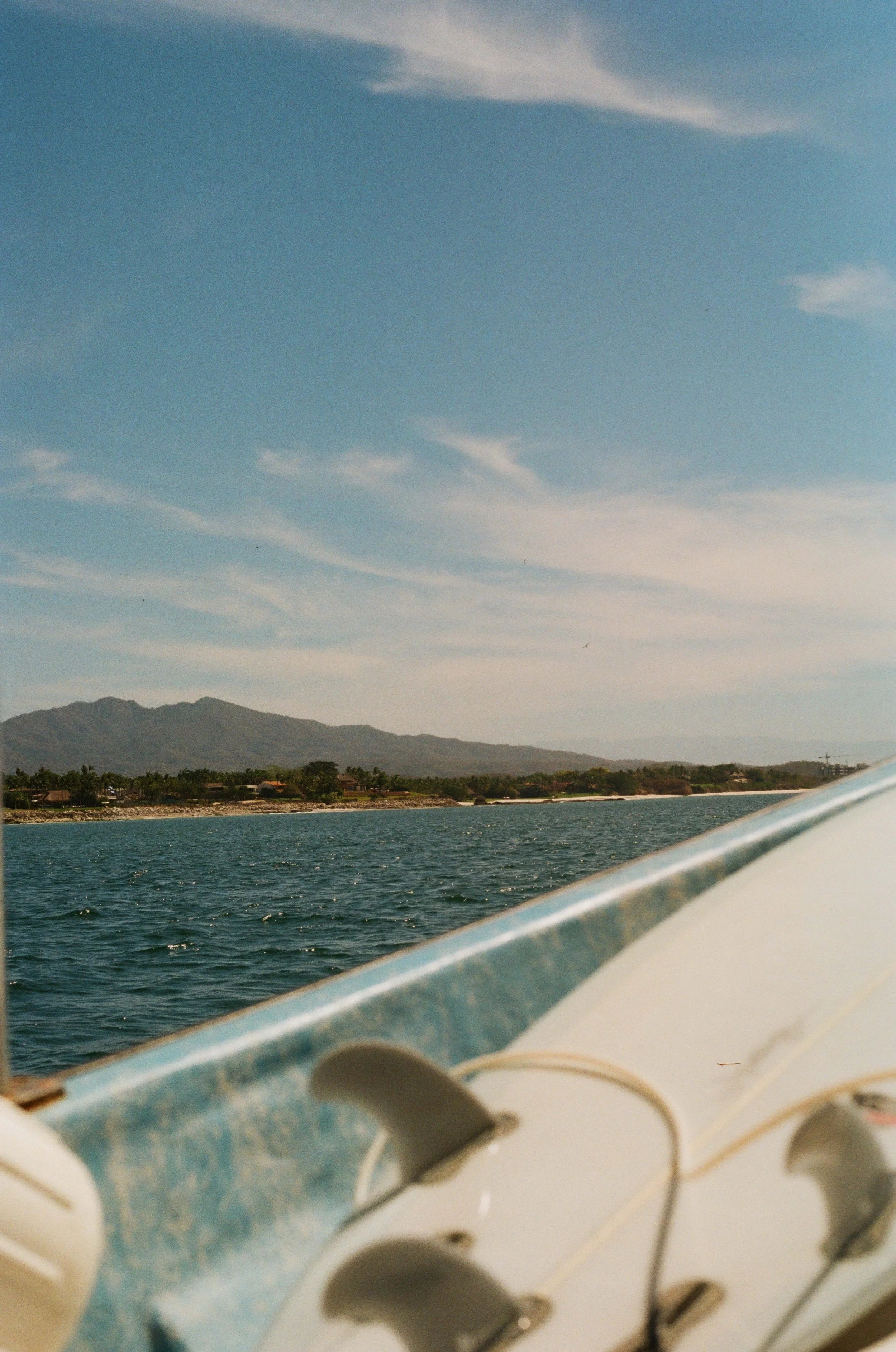 View of a body of water with mountains in the background and a partly cloudy sky, taken from a boat with metal and white plastic parts visible in the foreground.