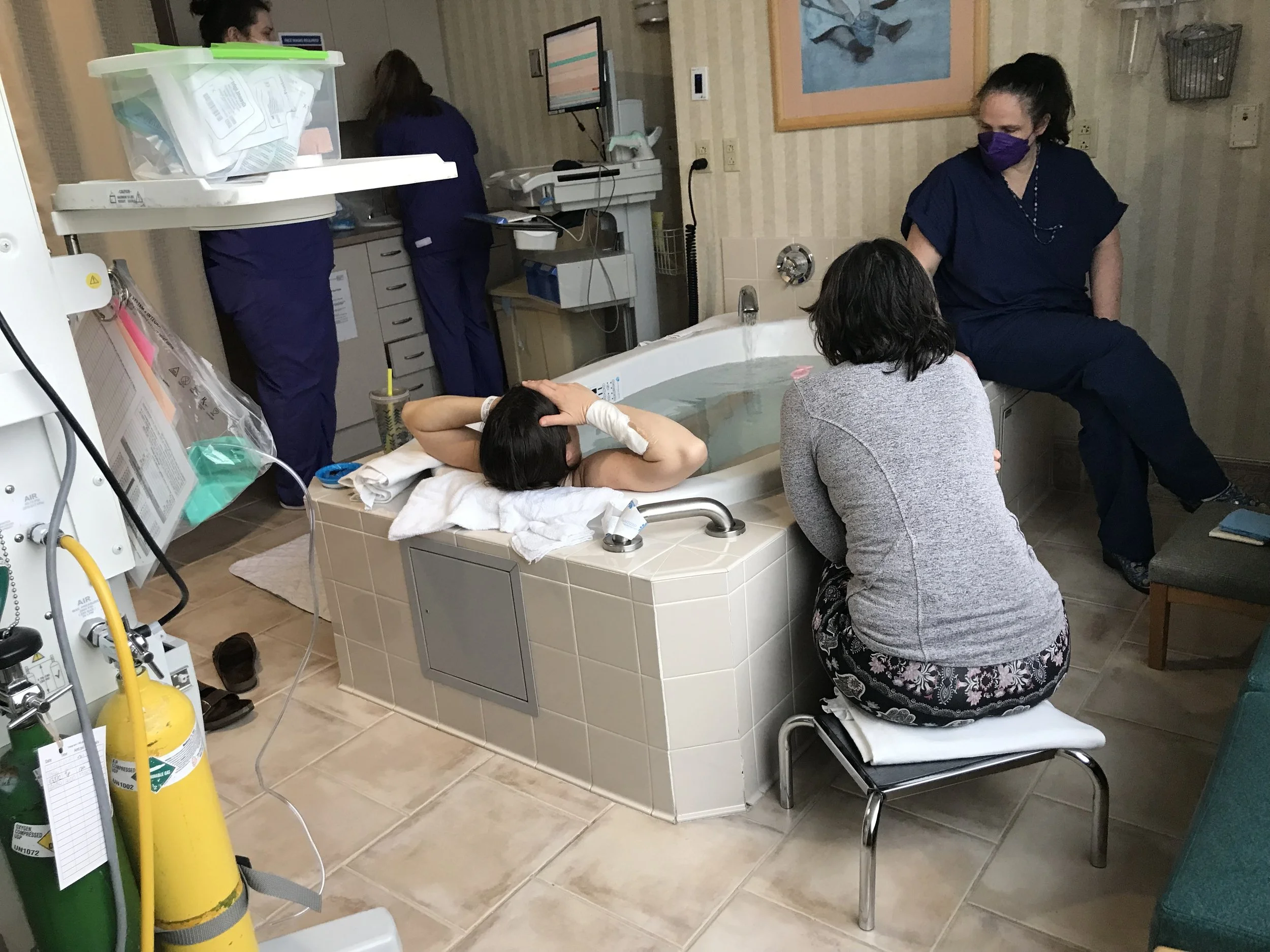 Woman birthing in a tub with doula and midwife using hypnobirthing techniques