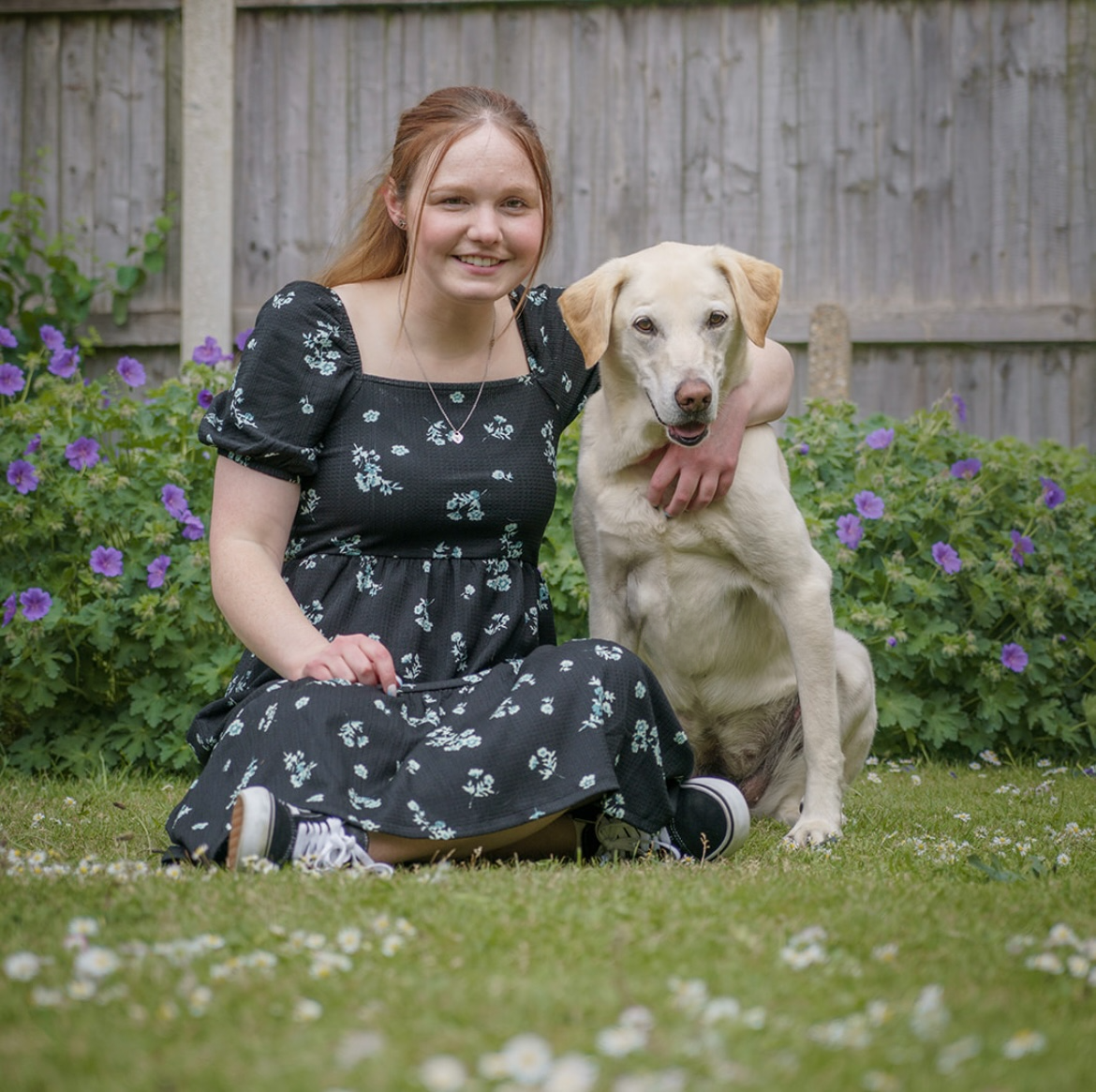 Female and yellow labrador smiling at the camera in front of purple flowers