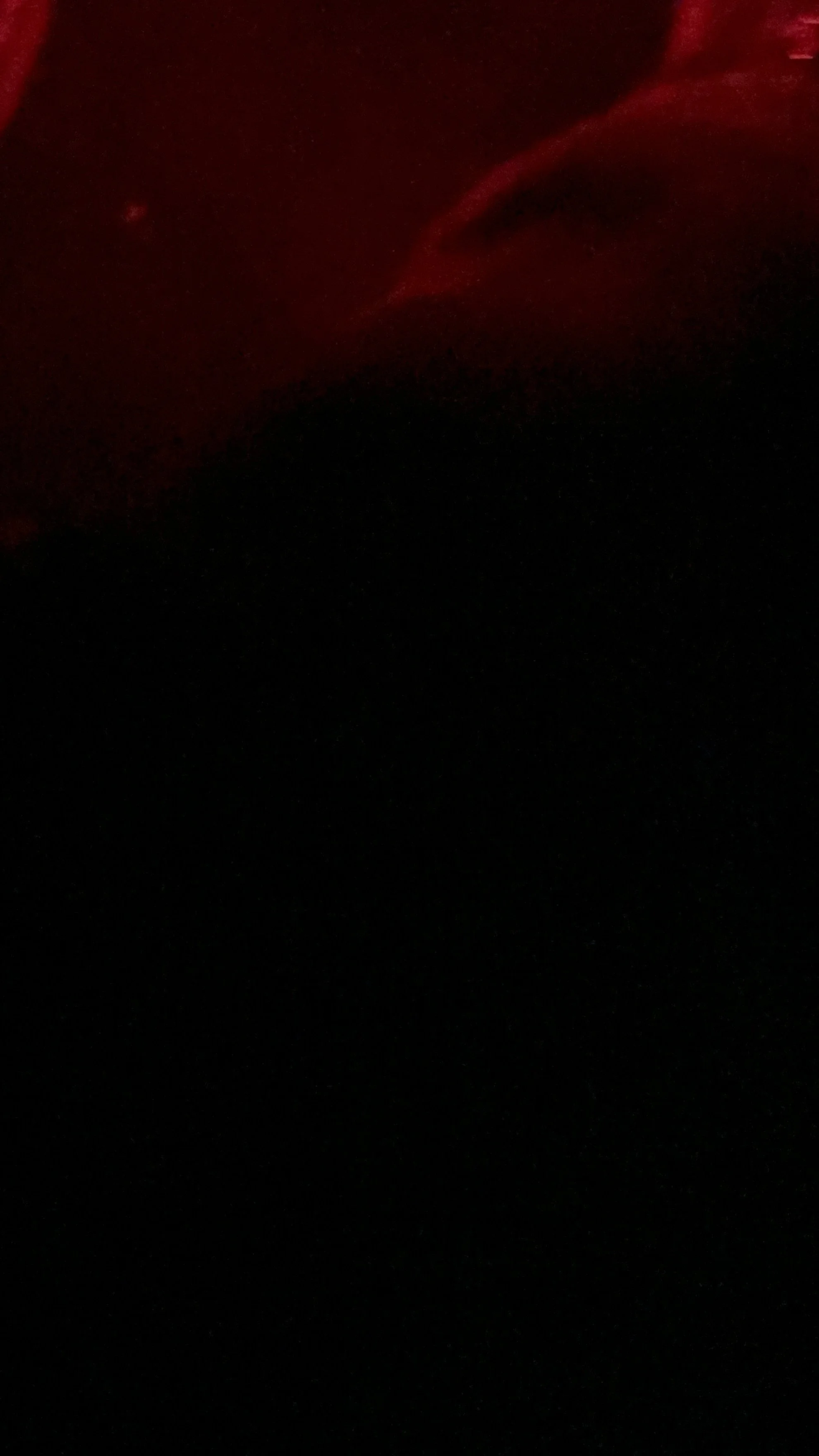Very dark image with a faint red glow or light in the upper left corner.