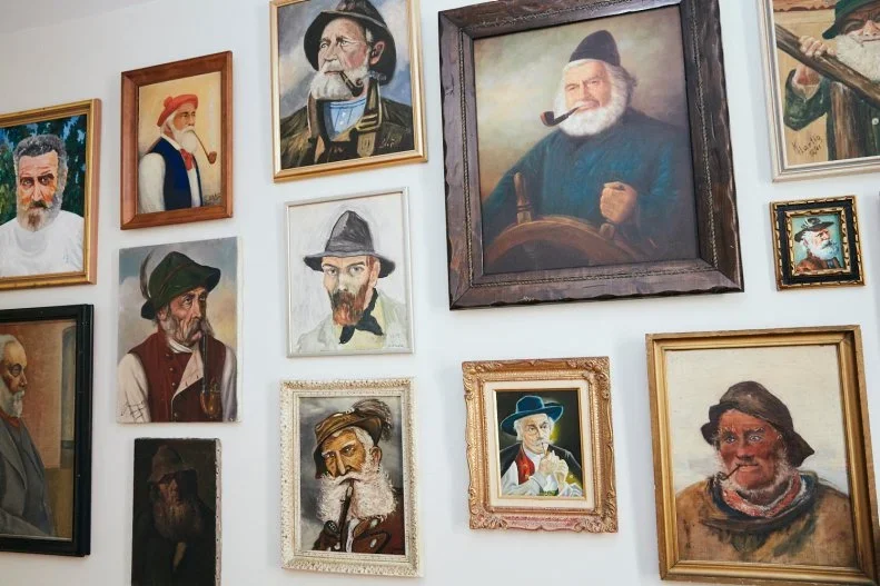 Wall decorated with various framed portrait paintings of historical figures, mostly men, in different styles and sizes.