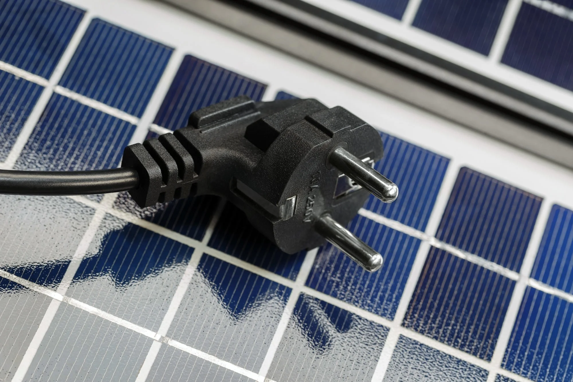 Close-up of a black power plug resting on solar panels with blue and silver cells.