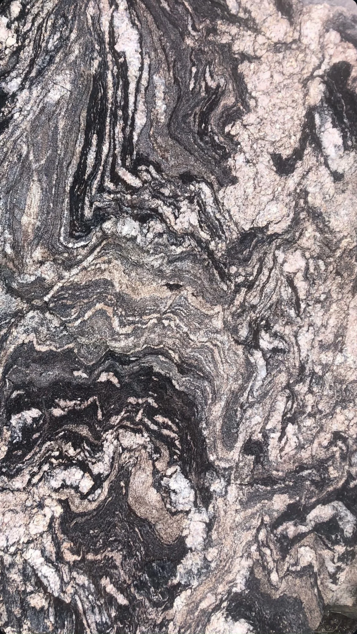 Close-up of a textured, swirling rock surface with black, gray, and light beige colors, showing intricate patterns and layers.