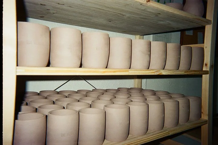 Unfinished ceramic pots on wooden shelves in a pottery studio.