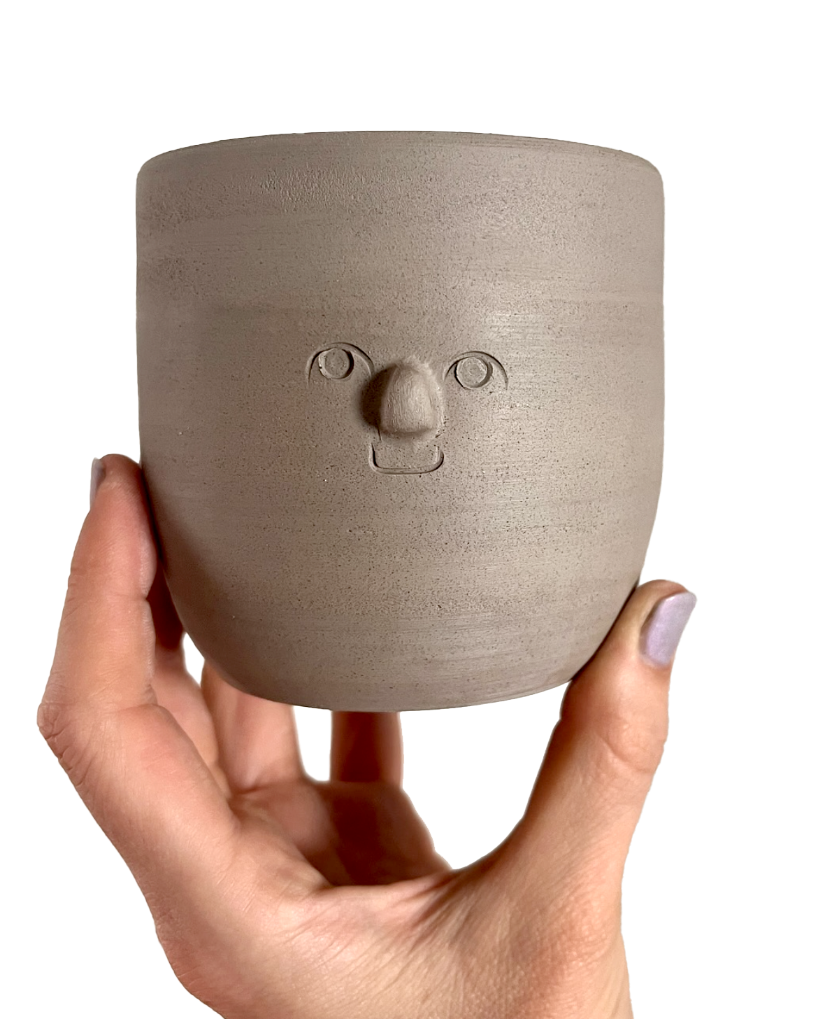 A beige ceramic pot with a face-shaped design, featuring carved eyes, nose, and mouth, being held by a person's hand.