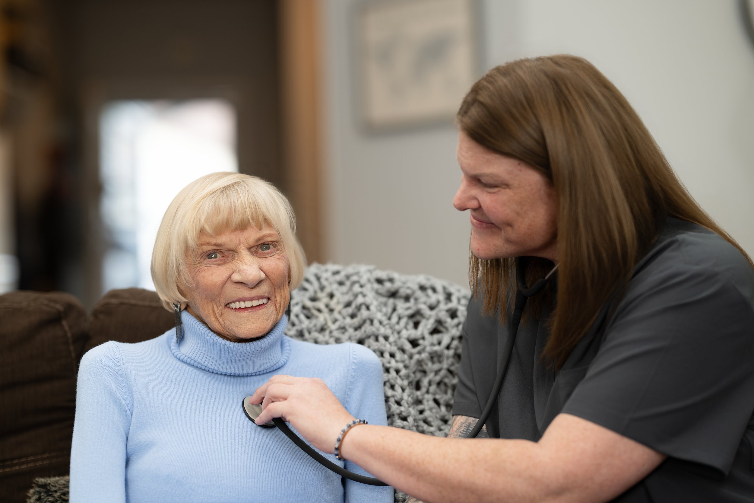 A nurse examining an elderly woman with a stethoscope in a cozy home setting.