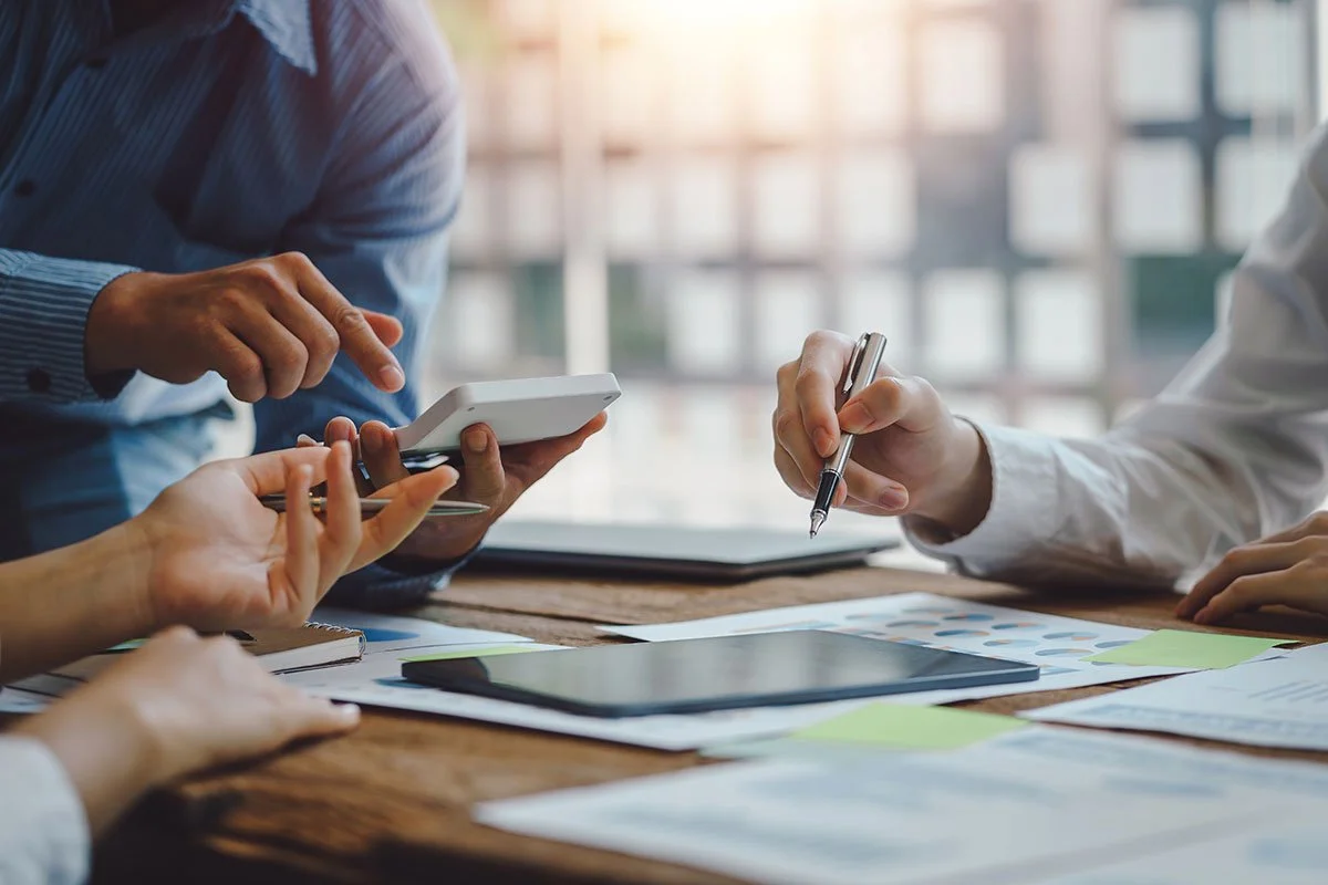 People working together at a table with a smartphone, pen, and documents.