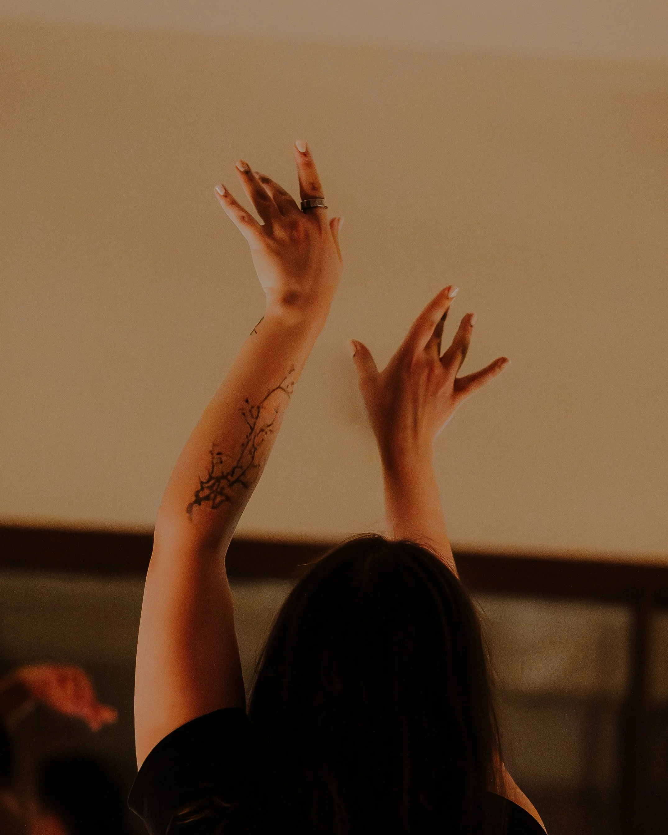 Person with outstretched arms and tattoos reaching towards the ceiling, with a beige background.