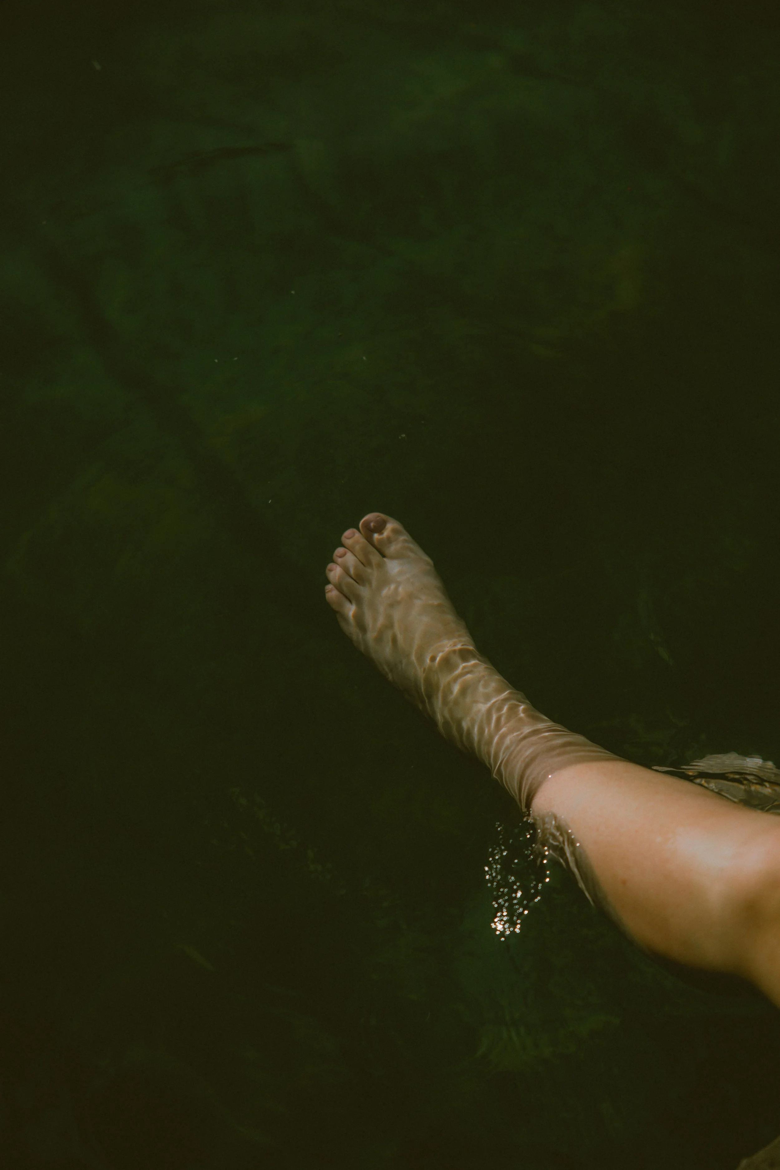 Zintuiglijke ervaring tijdens een sorae retreat; een detailopname van een been in het natuurlijke water van een zwemvijver, symbool voor verkoeling en vertraging.