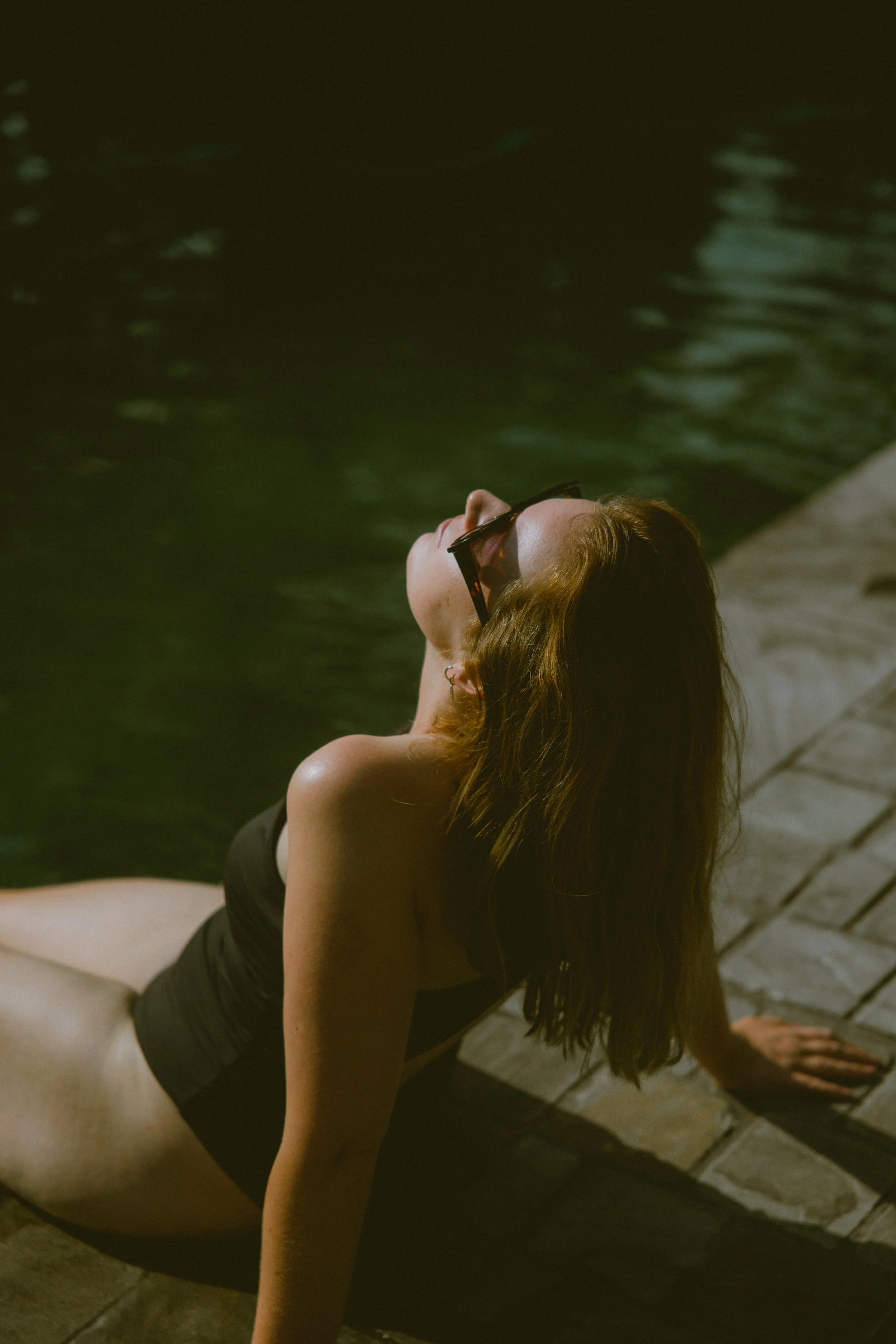 Femke van sorae genietend van de zon bij een natuurlijke zwemvijver; een moment van rust, aarding en verbinding met het lichaam.