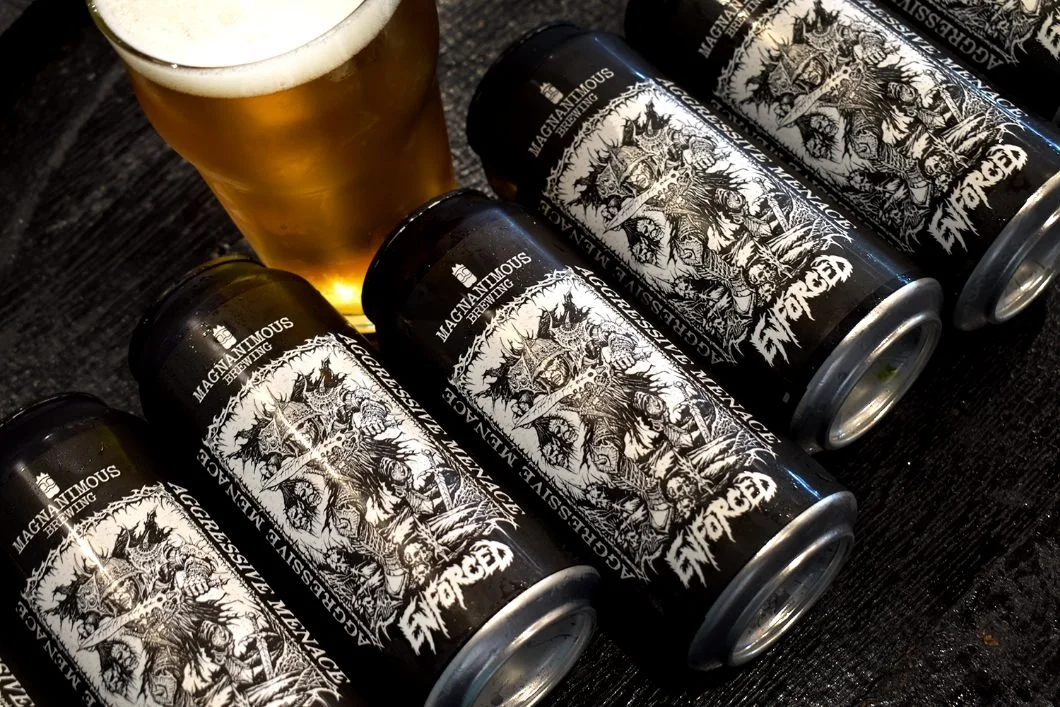 Six cans of Gorgon beer from Magnanimous Brewing arranged on a dark surface with a glass of beer nearby.