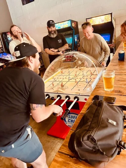 Adults drinking beer and cheering on friends playing bubble hockey