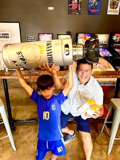 Kid victoriously holding up Stanley keg trophy with parent