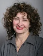 A woman with curly hair smiling, wearing a dark blazer.