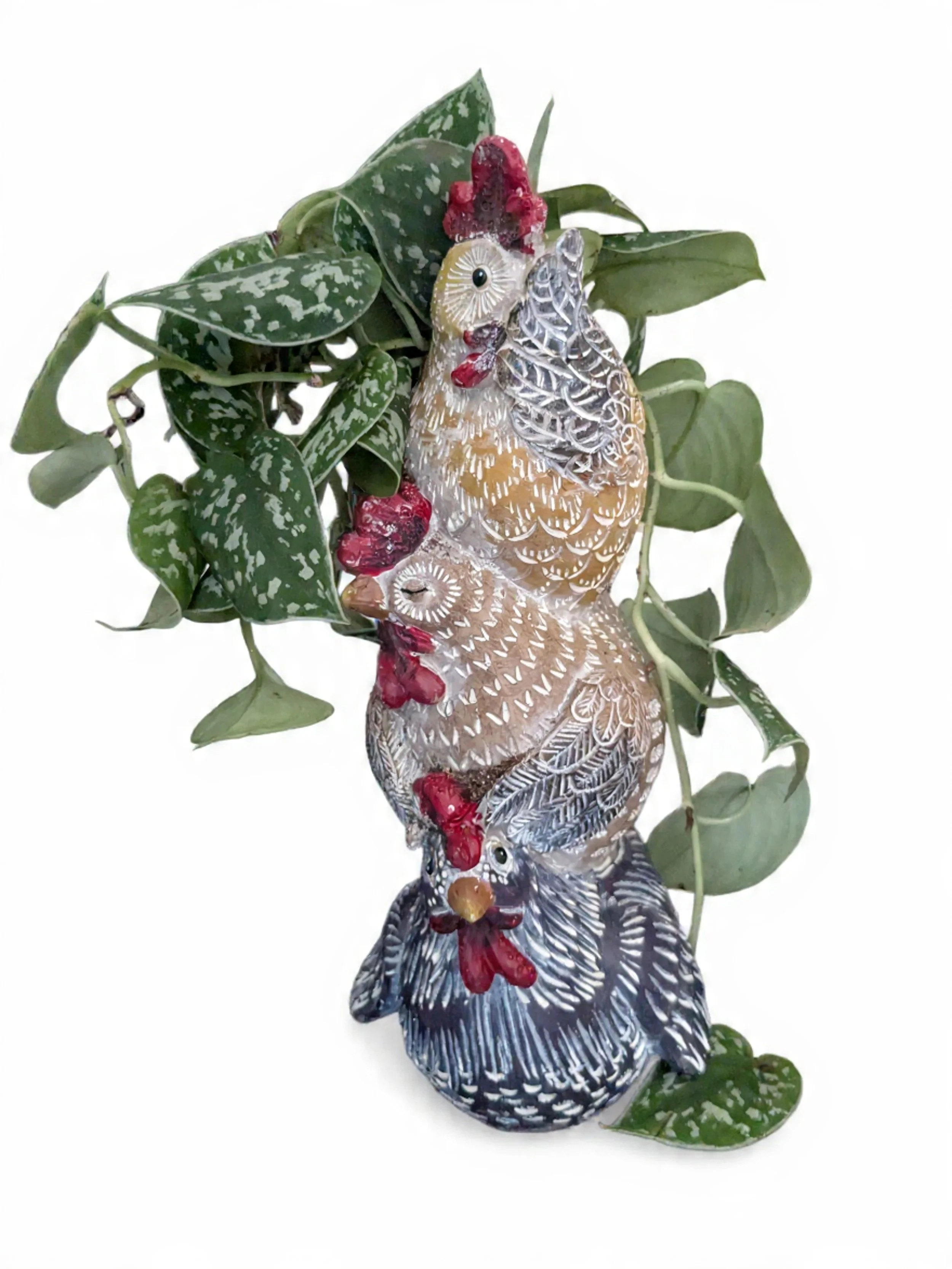 Decorative rooster and hen figurines intertwined with green leafy plants against a white background.