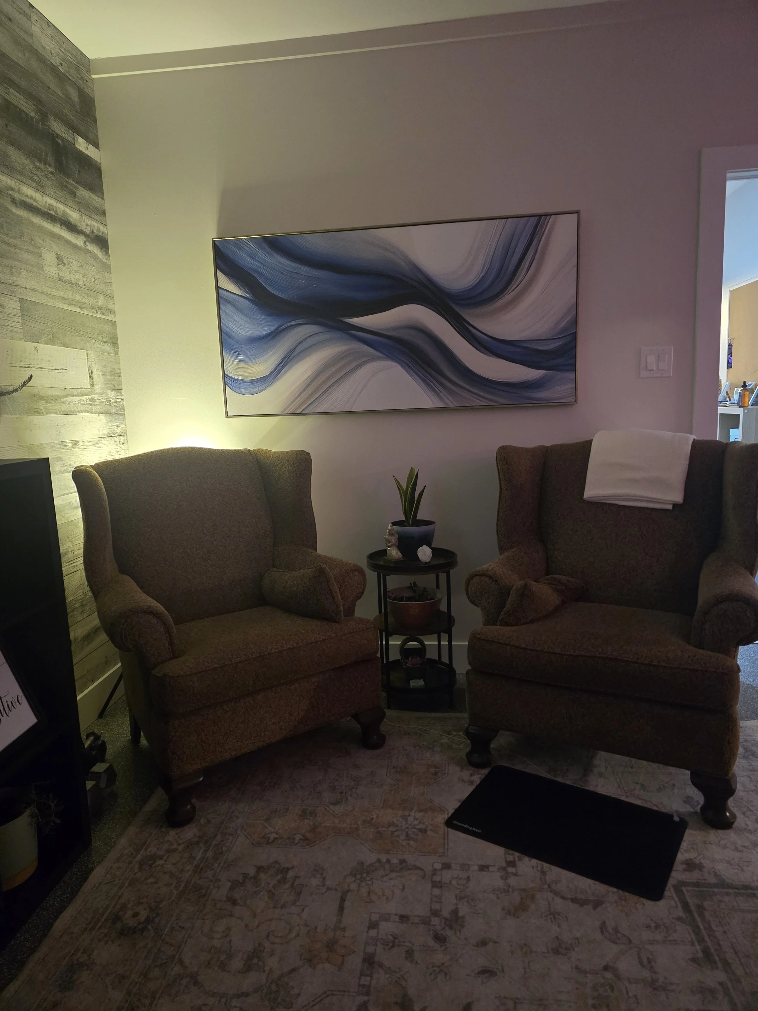Living room with two armchairs, a small side table with a potted plant, and abstract art on the wall.