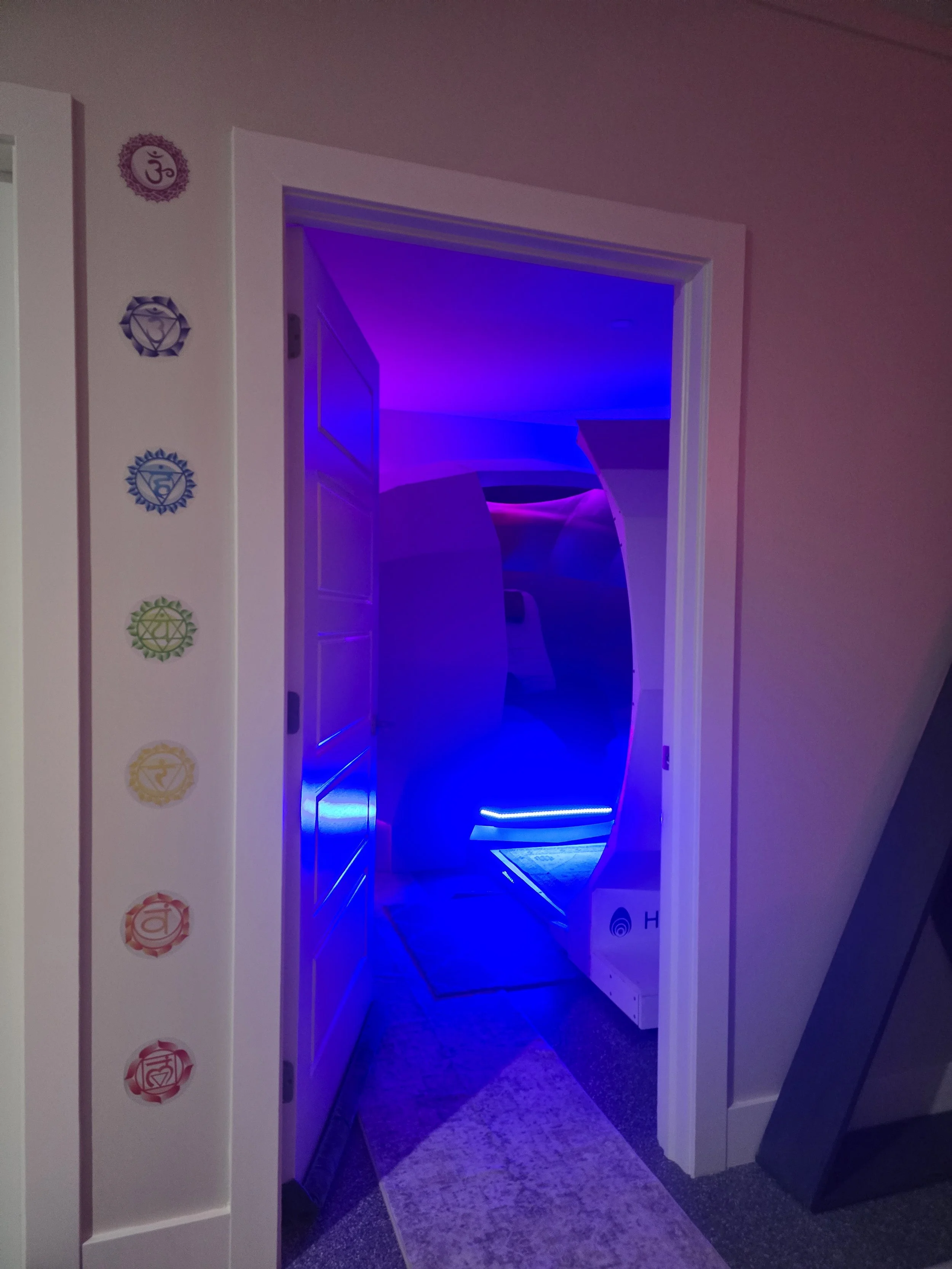 A doorway with a modern, curved, illuminated installation visible through the doorframe. The room is lit with blue and purple neon lights.