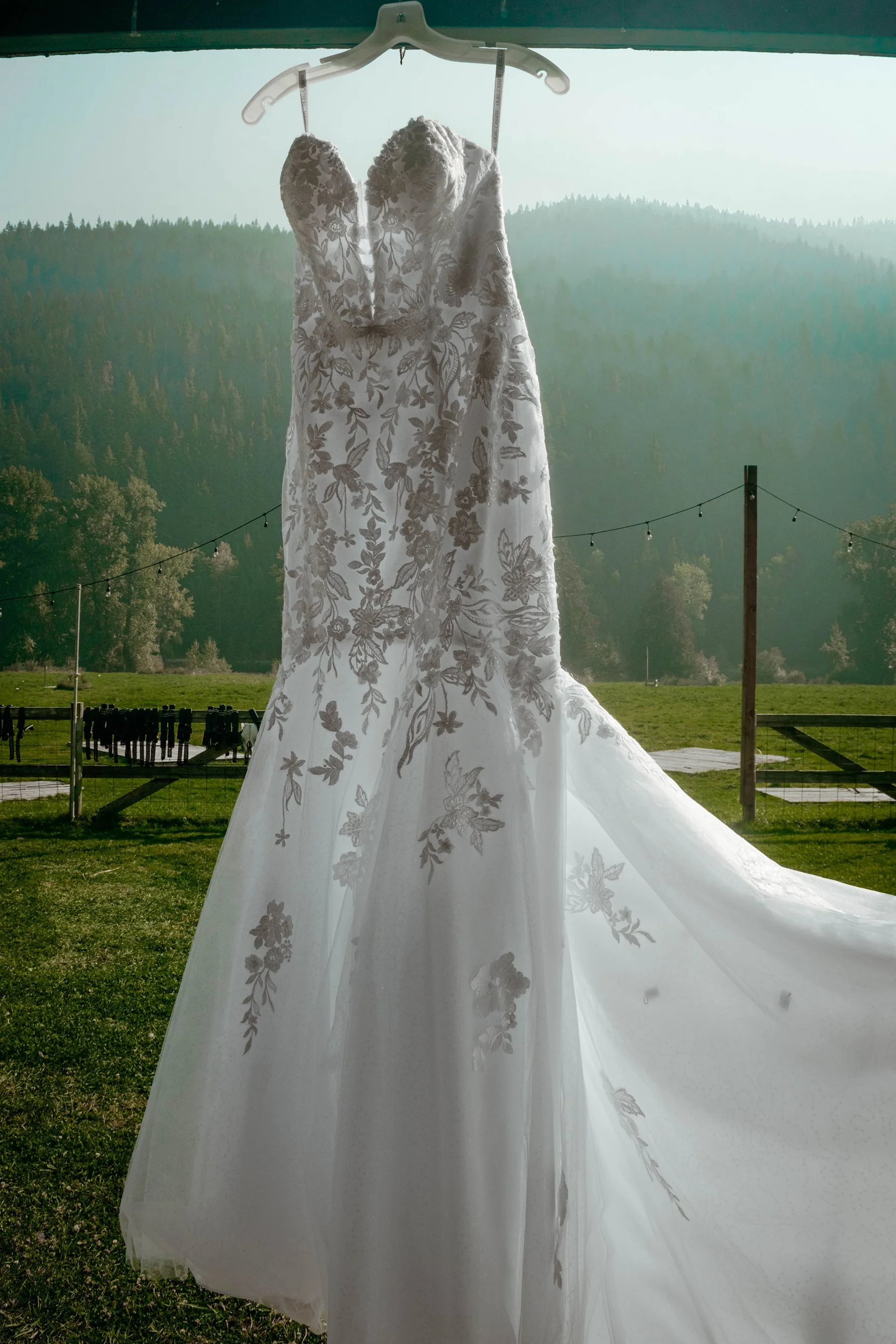 A wedding dress hanging on a hanger outdoors with a mountainous landscape in the background.
