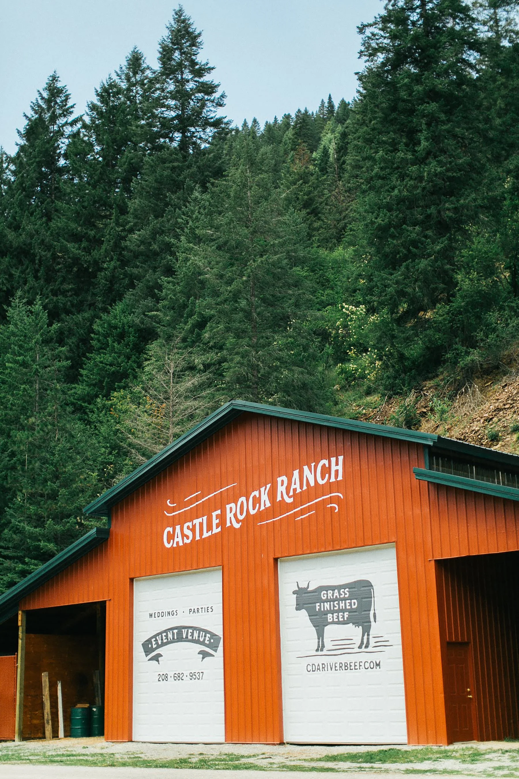 Orange barn with white signs advertising upcoming weddings and parties at Castle Rock Ranch, with green forested hills in the background.