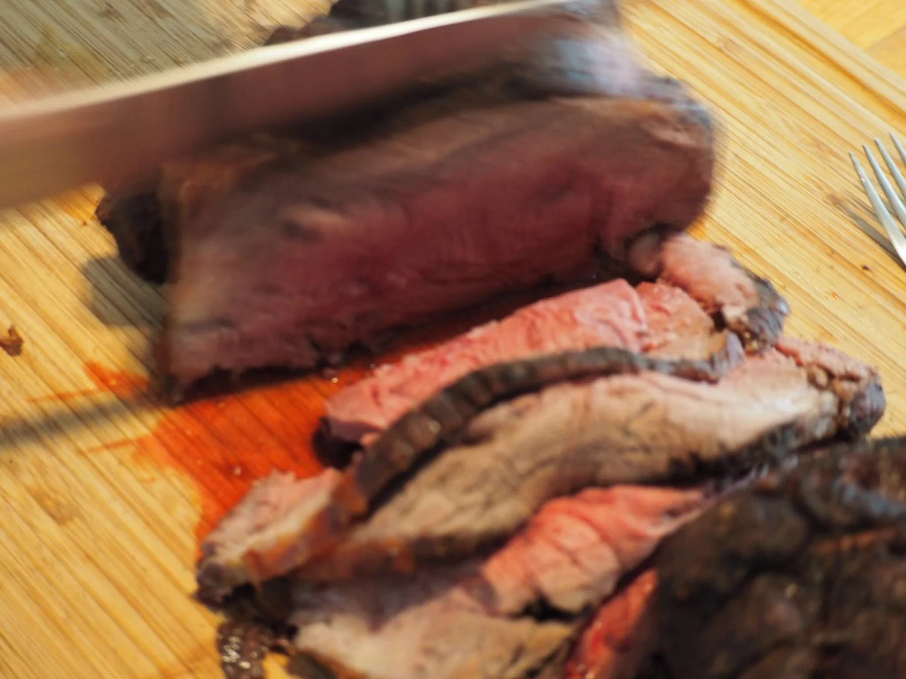 Sliced cooked steak on a wooden cutting board with a fork nearby.