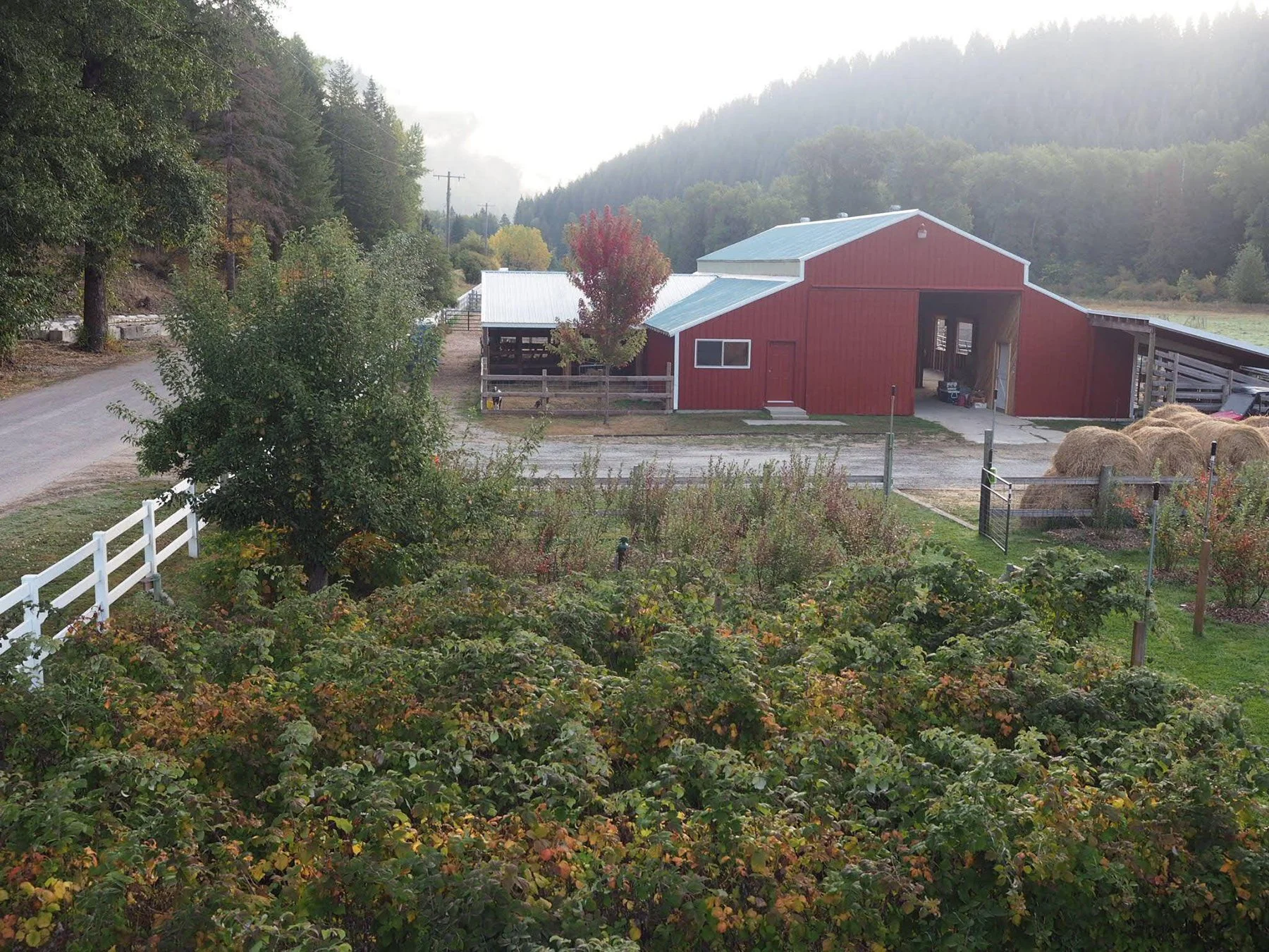A rural farm scene with a red barn, hay bales, and surrounding trees and hills.