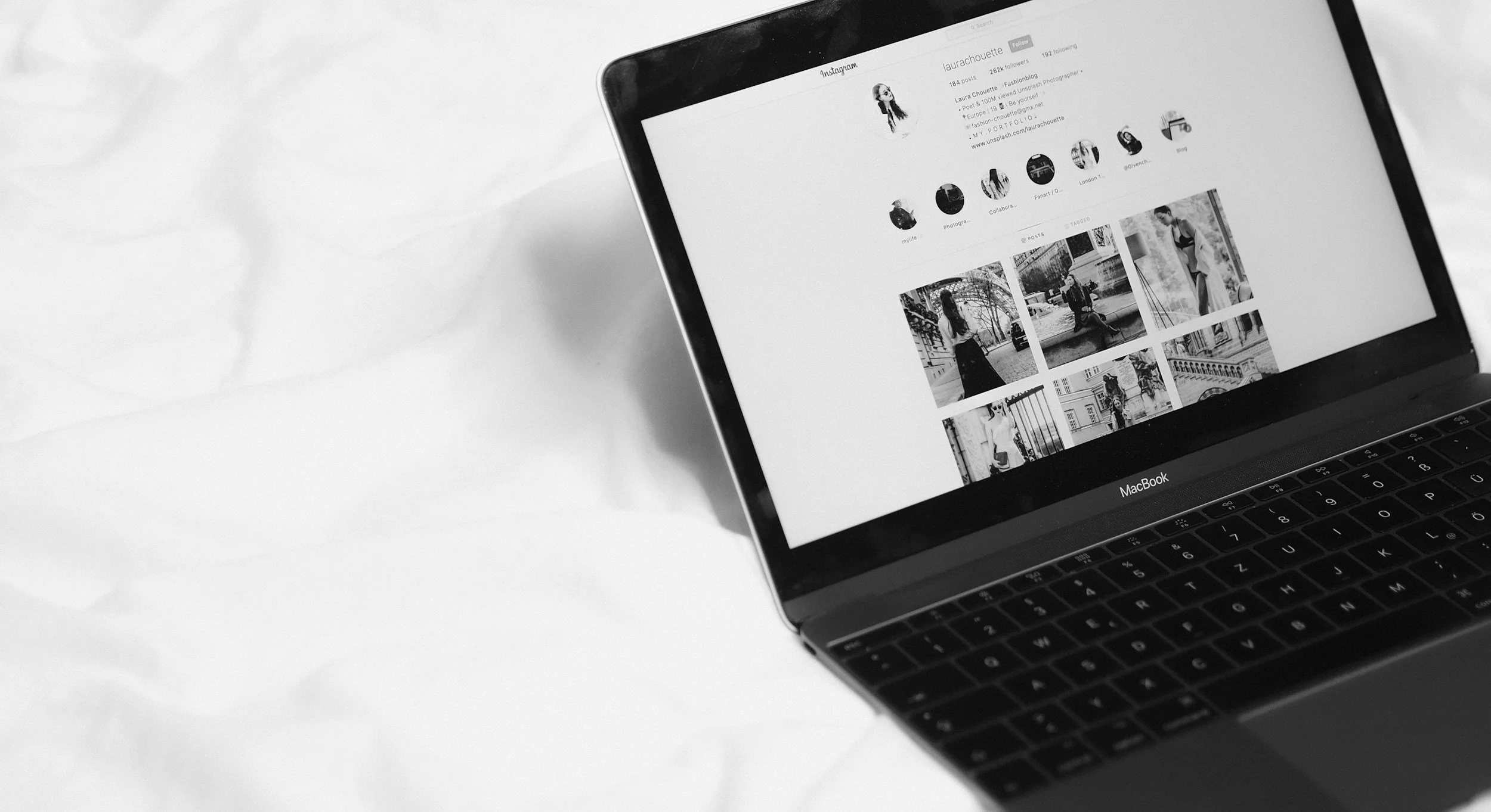 A MacBook laptop on a white surface displaying an Instagram profile with photos.
