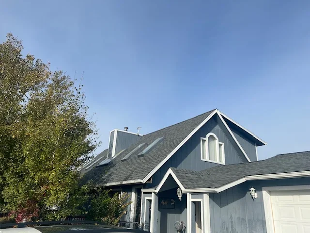Front view of a two-story North Idaho home with a dark gray asphalt shingle roof under clear skies.