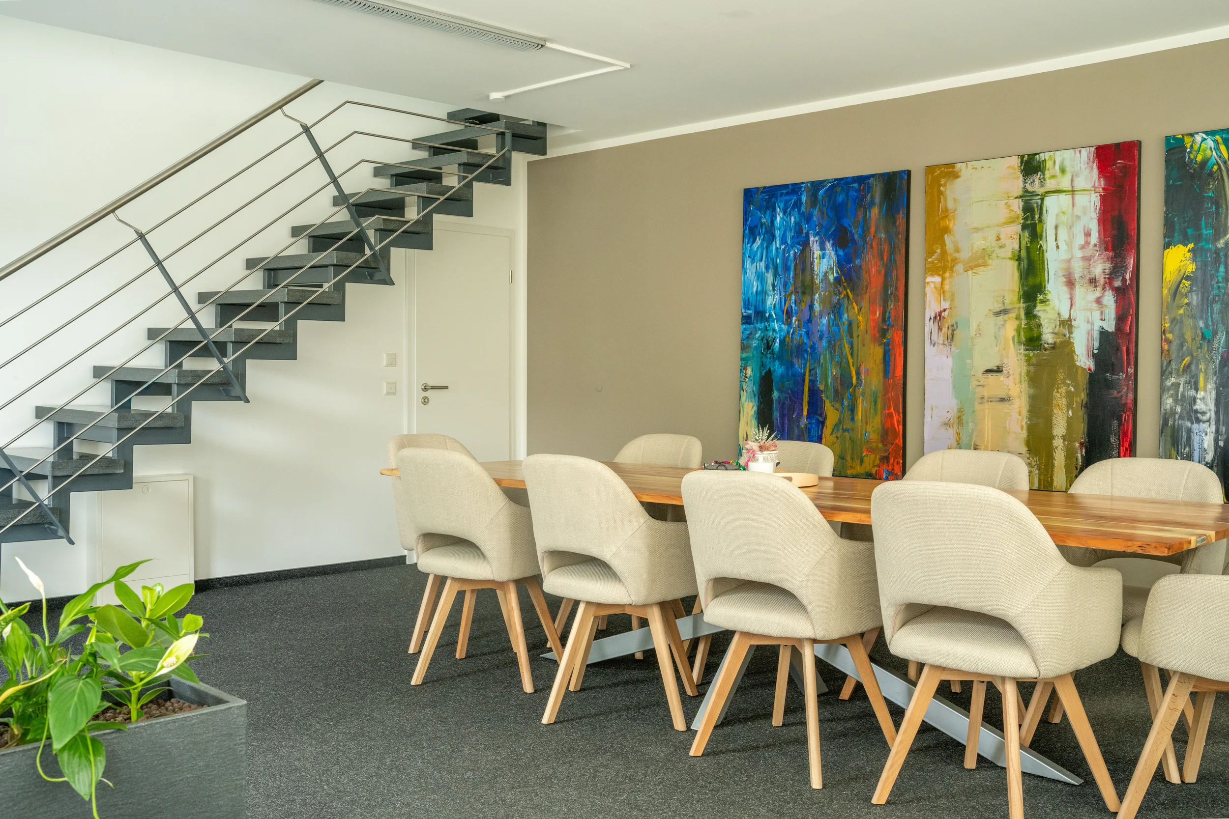 Moderner Seminarraum in Münster mit Holztisch, Sitzgruppe, moderner Kunst und einer Design-Metalltreppe. Ideal für exklusive Firmenevents und Workshop-Formate in stilvollem Ambiente.